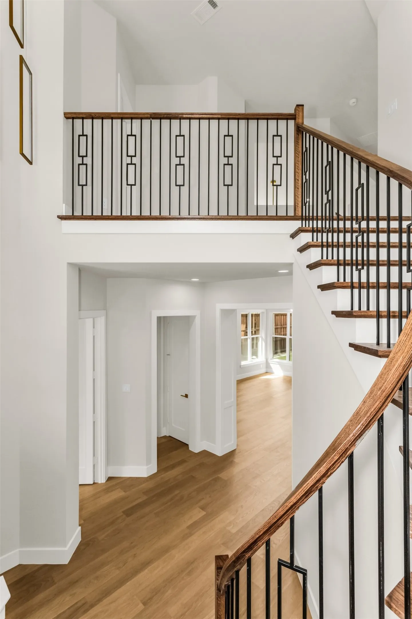 Two-story entry with wood-finish flooring, a curved staircase with wrought iron balusters, and a second-story landing featuring a matching railing