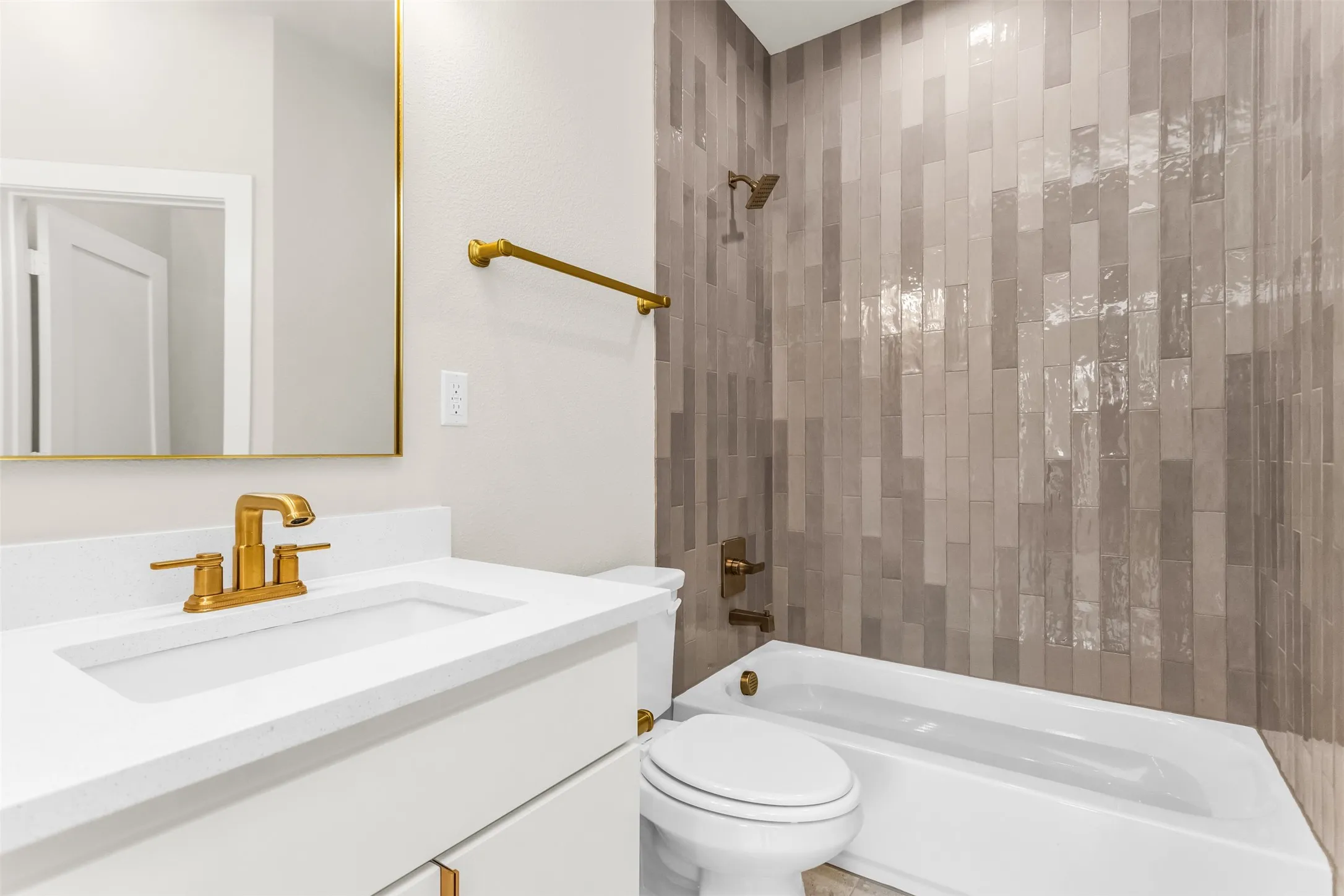 Bathroom featuring a white vanity with gold-finish fixtures, a framed mirror, a white bathtub, and a shower with vertical tile detailing