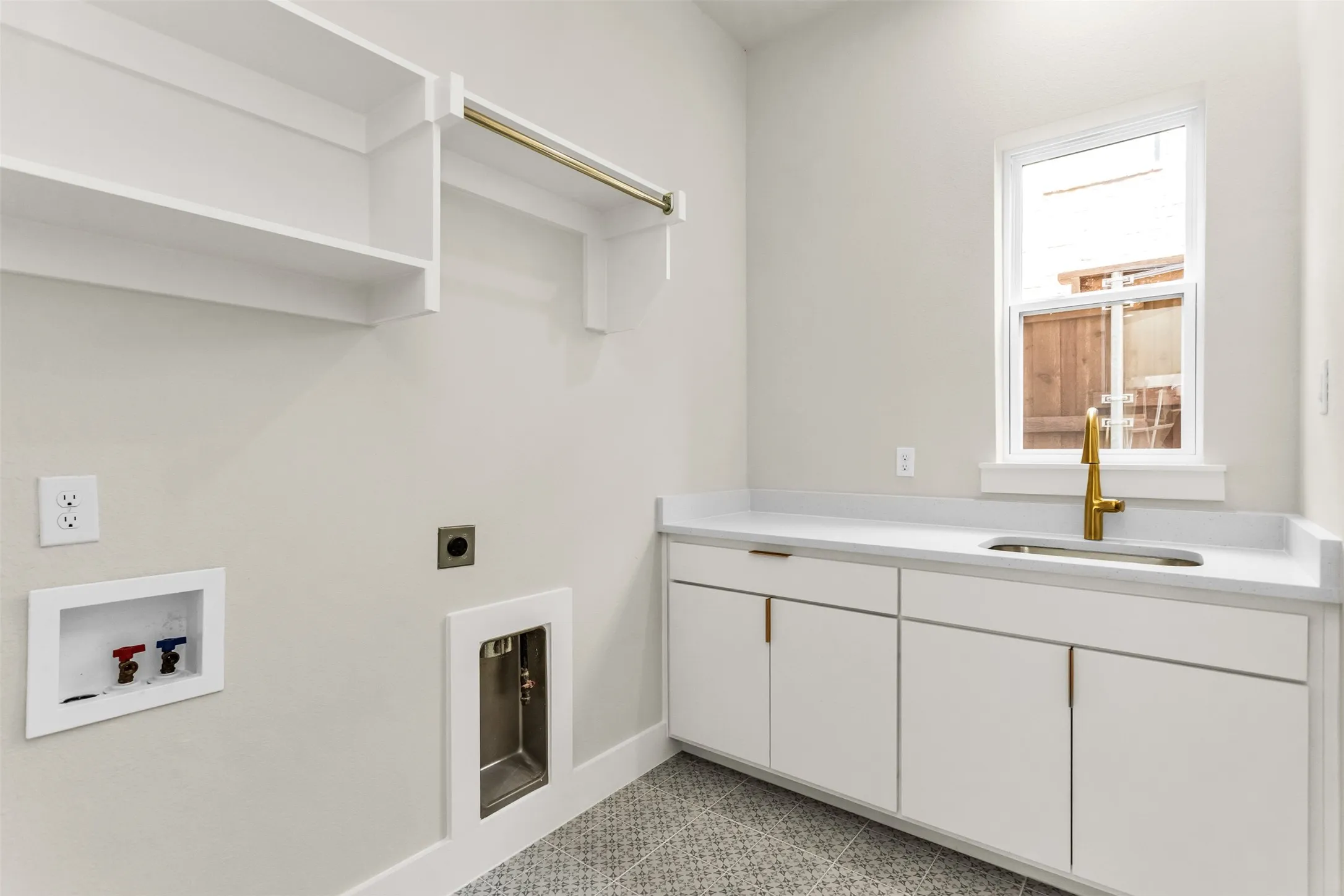 Laundry room featuring white cabinetry, a built-in sink with a gold-tone faucet, a white countertop, and patterned floor tiling