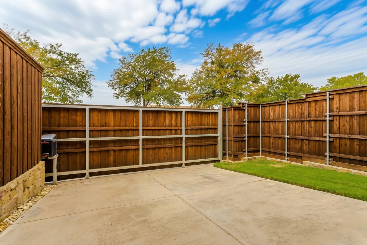 Expansive concrete patio with wood panel fencing and a grass area