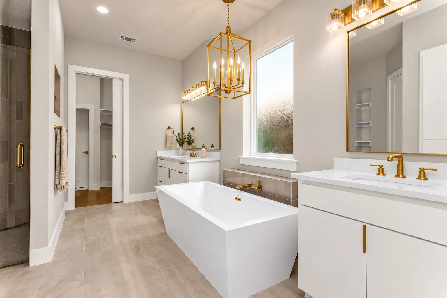 Freestanding soaking tub with gold-tone fixtures, dual vanities with white countertops and gold-tone hardware, tile flooring, and a glass-enclosed shower with gold-tone hardware
