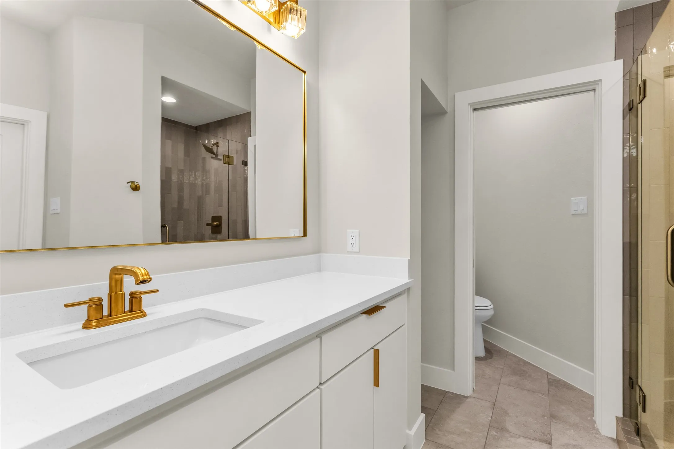 White vanity with gold-finish hardware, rectangular undermount sink, and solid surface countertop