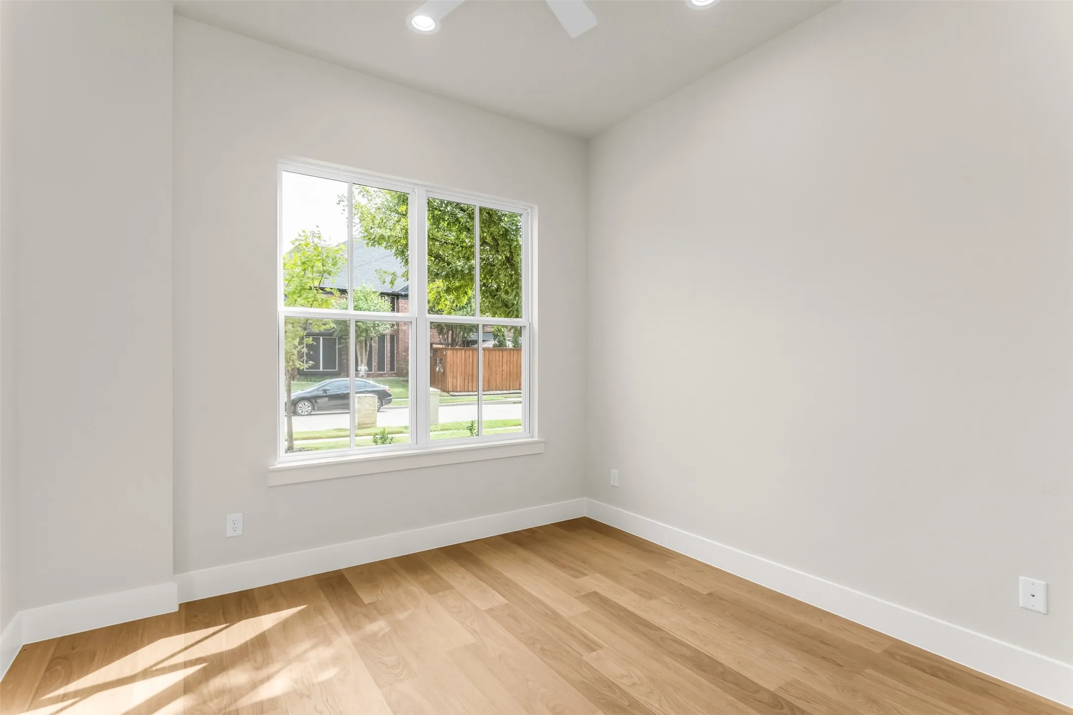 Recessed lighting, wood-finish flooring, white trim, and a window with white casing