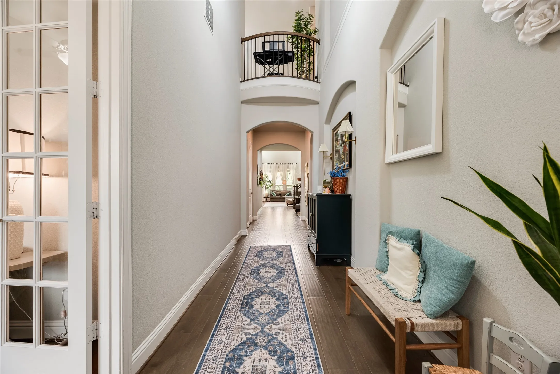 Double-height foyer featuring wood-finish flooring, an arched entryway, and a balcony with an ornate railing