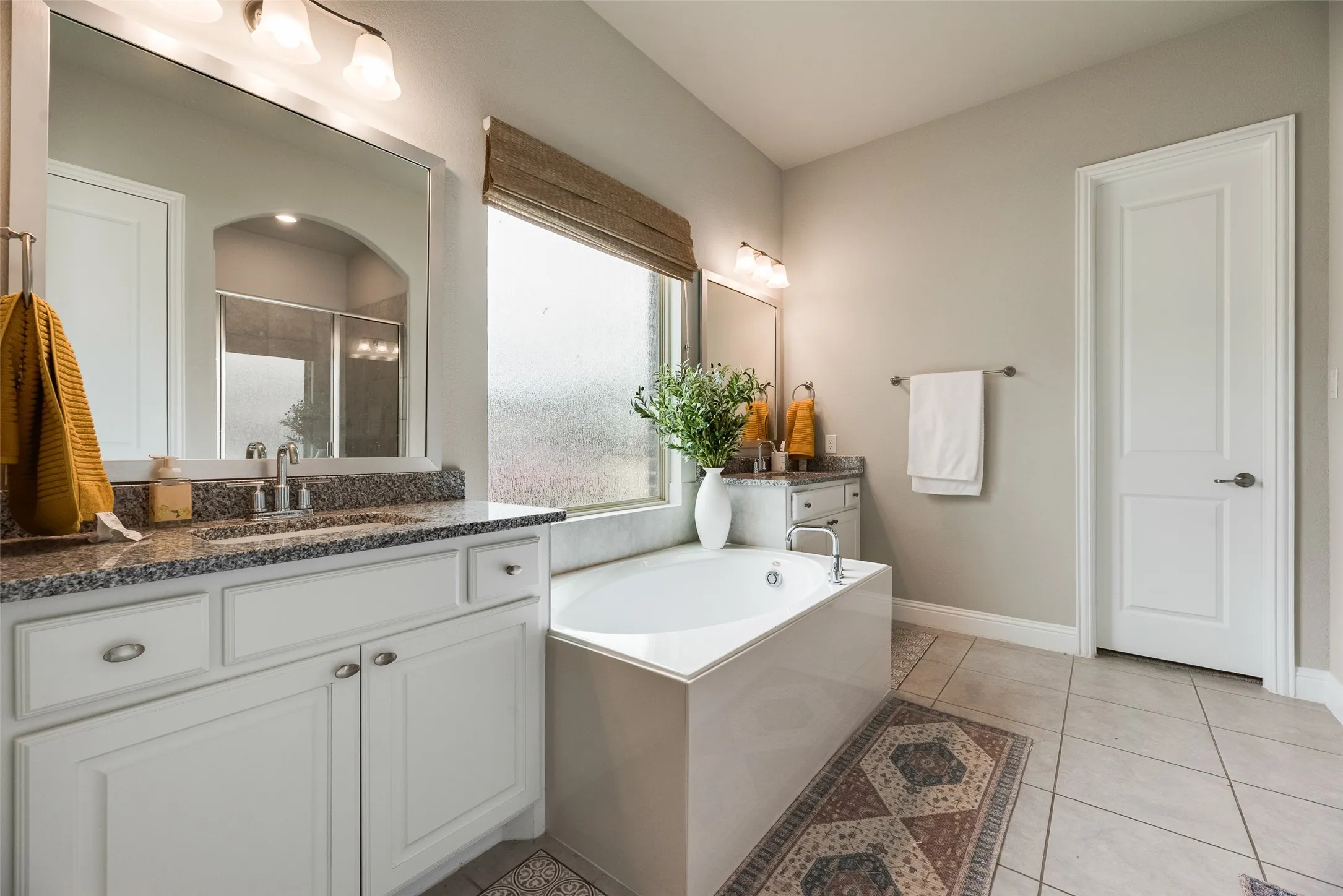 Dual vanity with granite countertops, a built-in soaking tub, tile flooring, and a walk-in shower with a glass enclosure