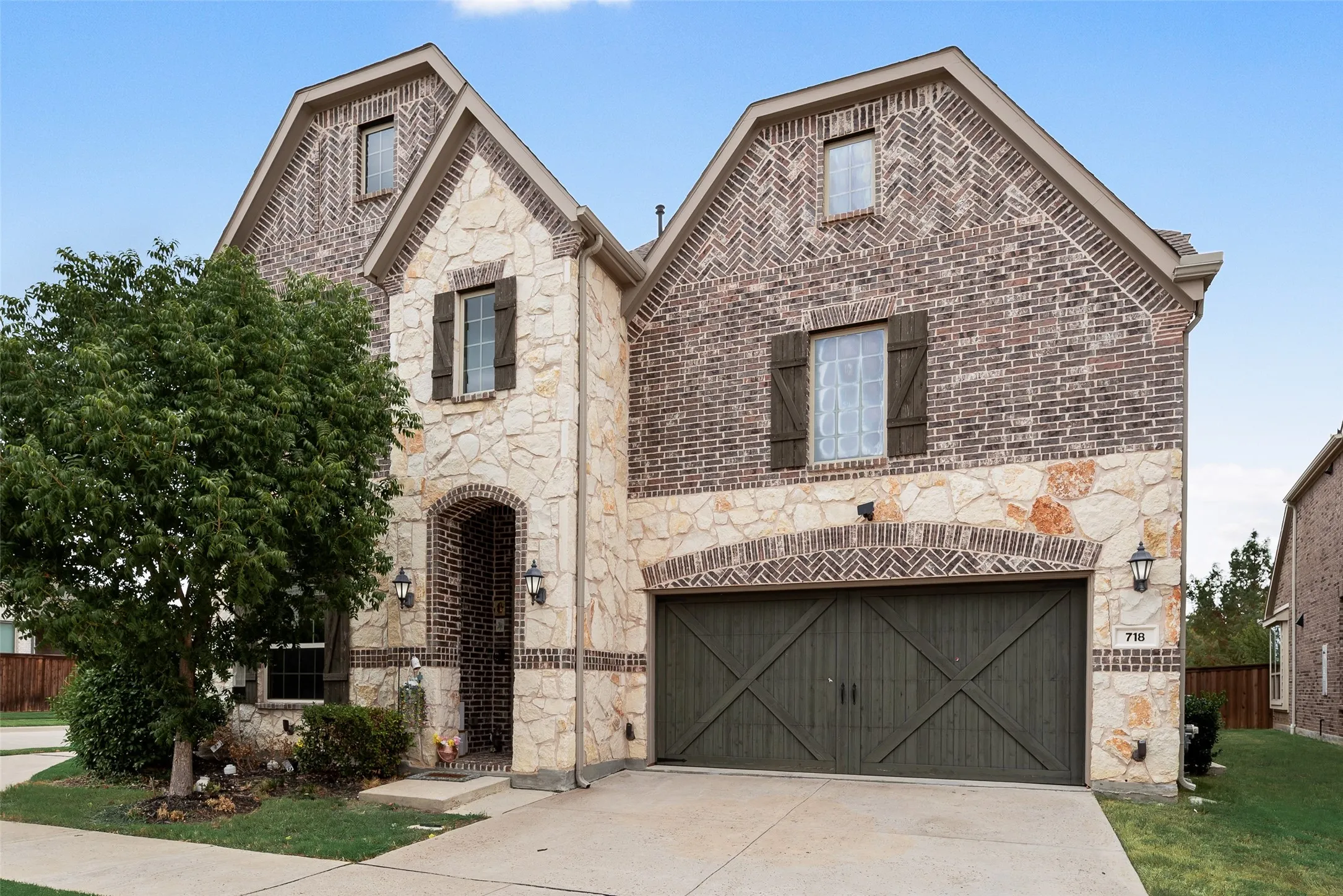Two-story exterior with a brick and stone facade, arched entry, decorative window shutters, and a two-car garage with barn-style doors