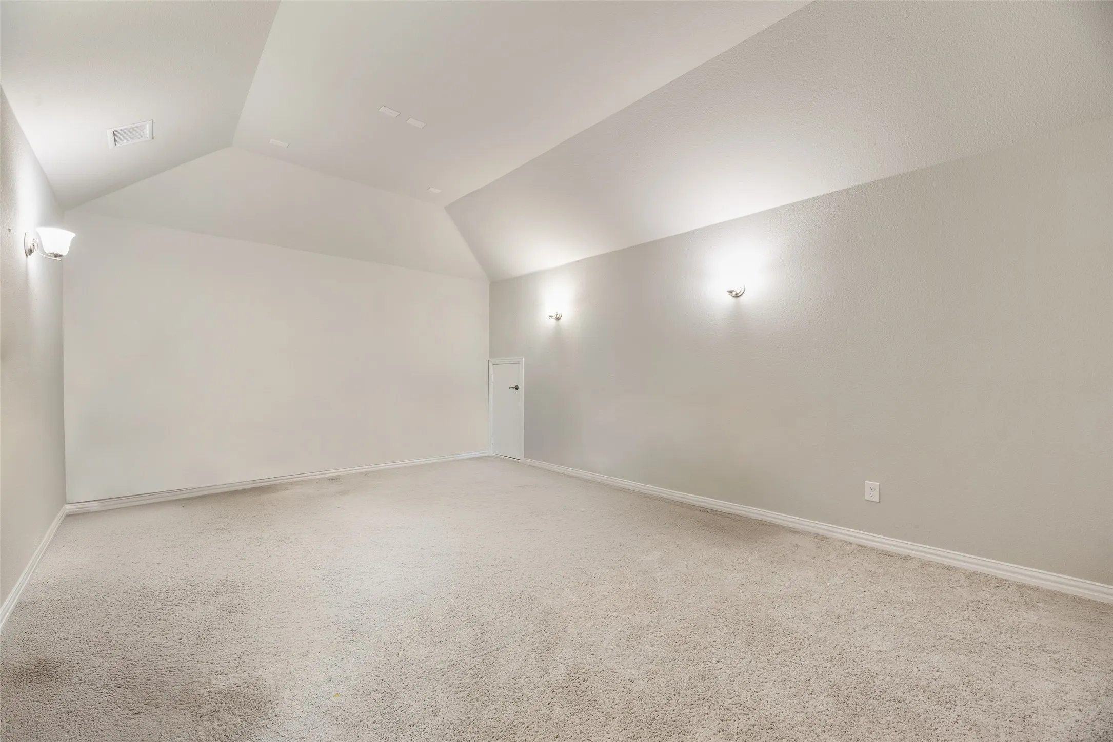 Carpeted flooring, vaulted ceiling, white walls, wall sconces, and a white door