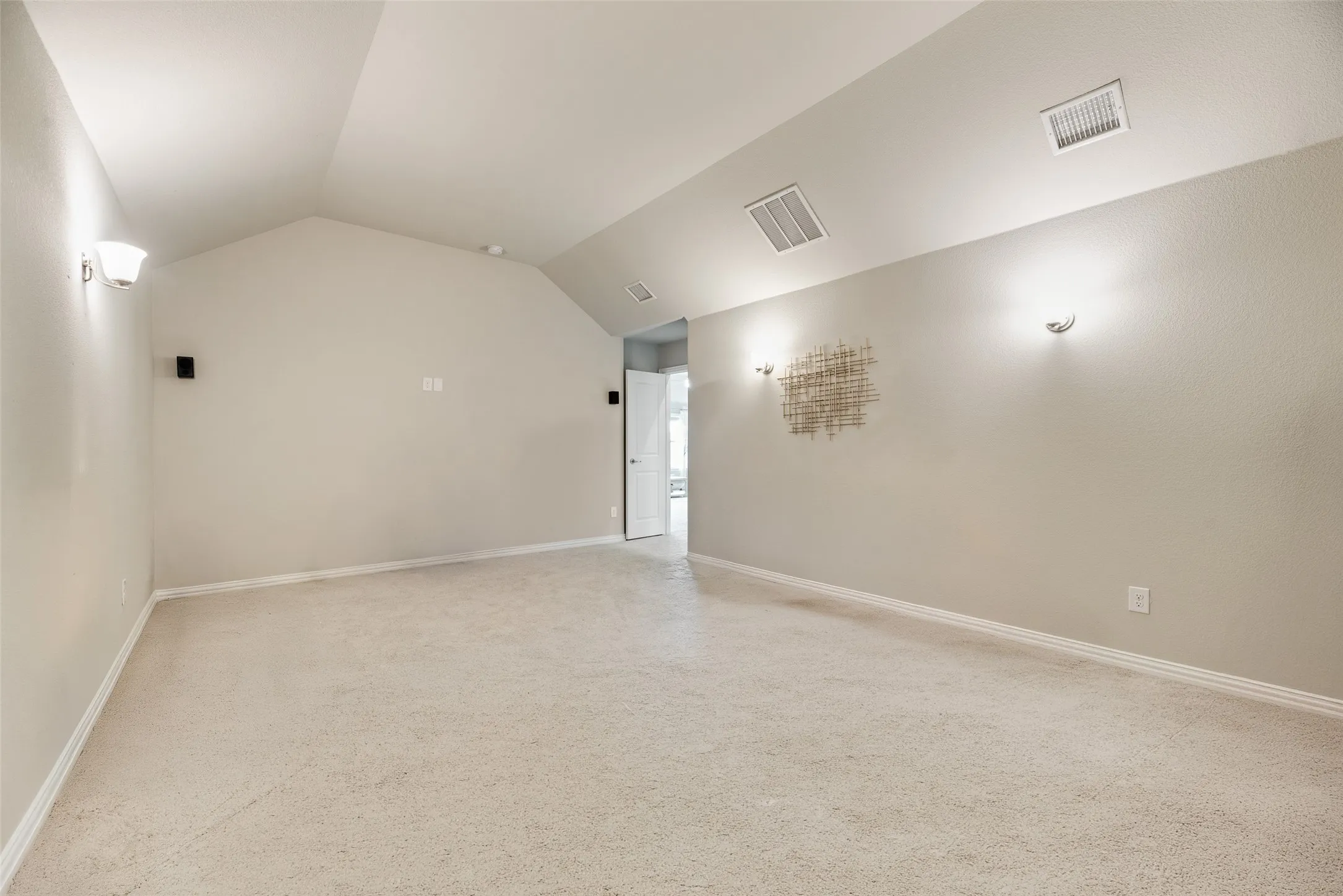 Carpeted room featuring a vaulted ceiling and wall-mounted sconces