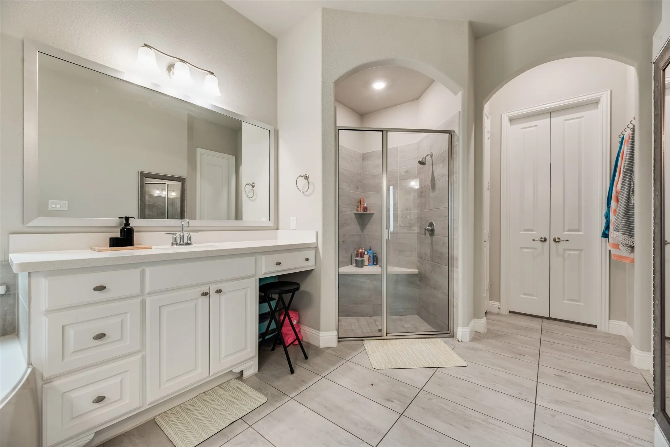 Bathroom featuring a double-door closet, a vanity with ample counter space, an integrated sink, and a walk-in shower with a built-in bench