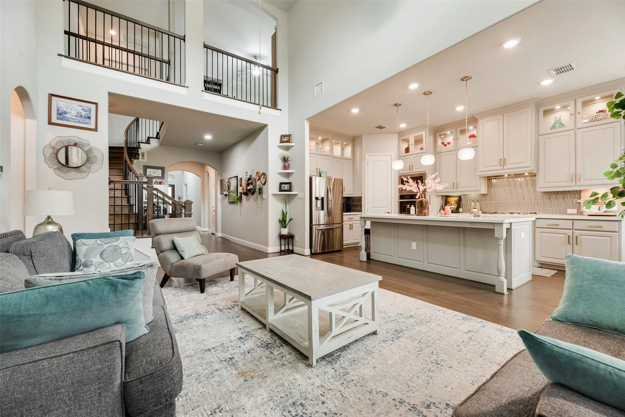 Two-story great room with a spiral staircase, wood-finish flooring, and a kitchen featuring a large island, pendant lighting, and stainless steel appliances