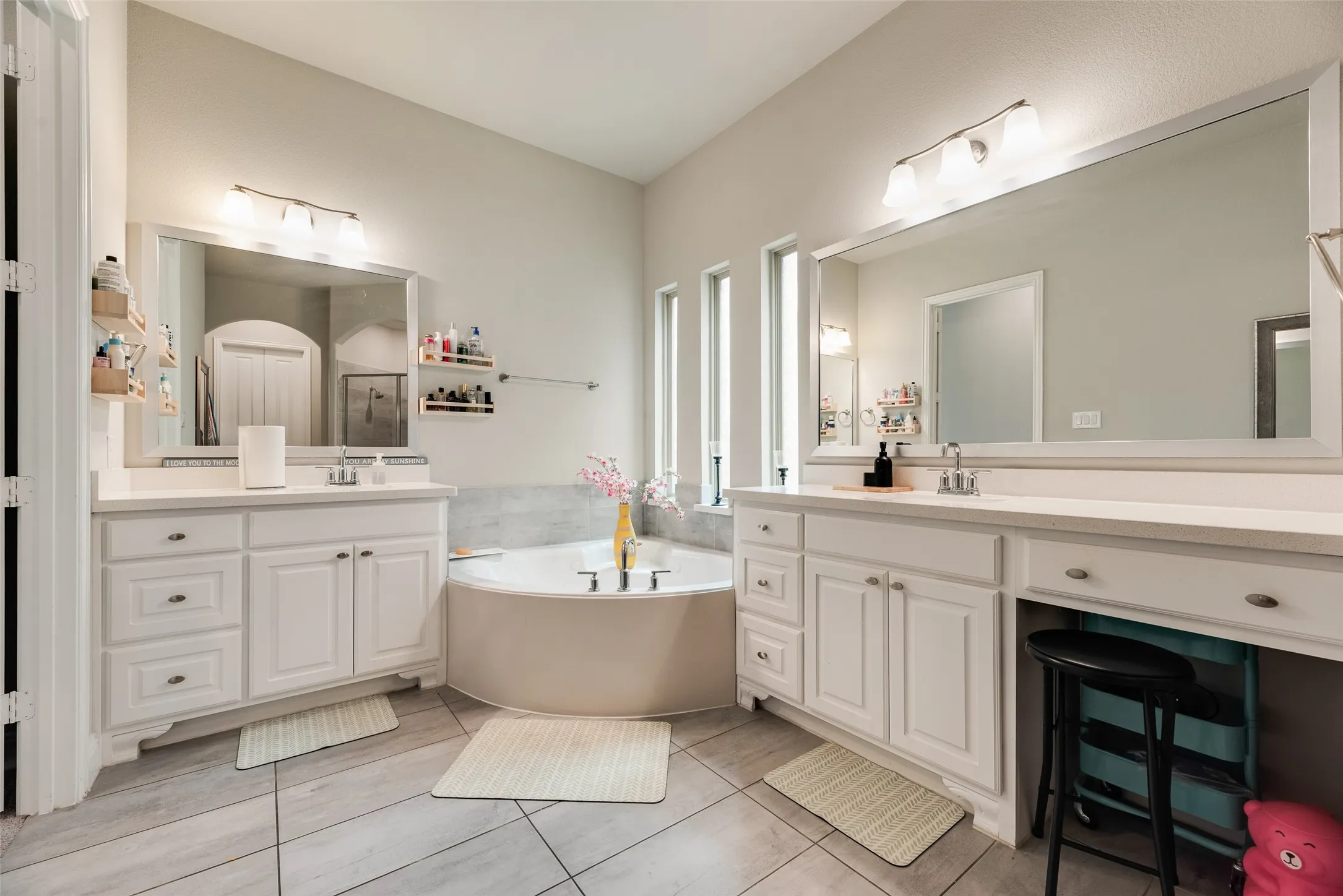 Dual vanity with white cabinetry, a built-in vanity, a corner bathtub, and vertical accent windows