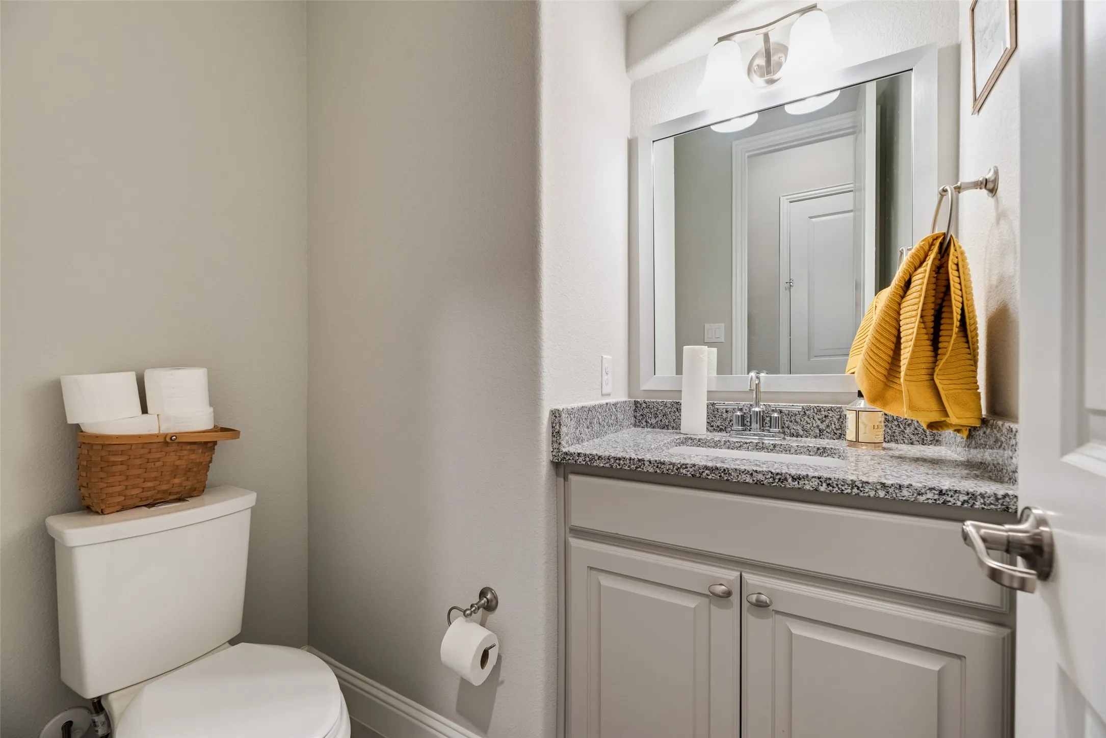 Vanity featuring a light gray shaker cabinet, speckled countertop, and wall-mounted mirror with an overhead light fixture