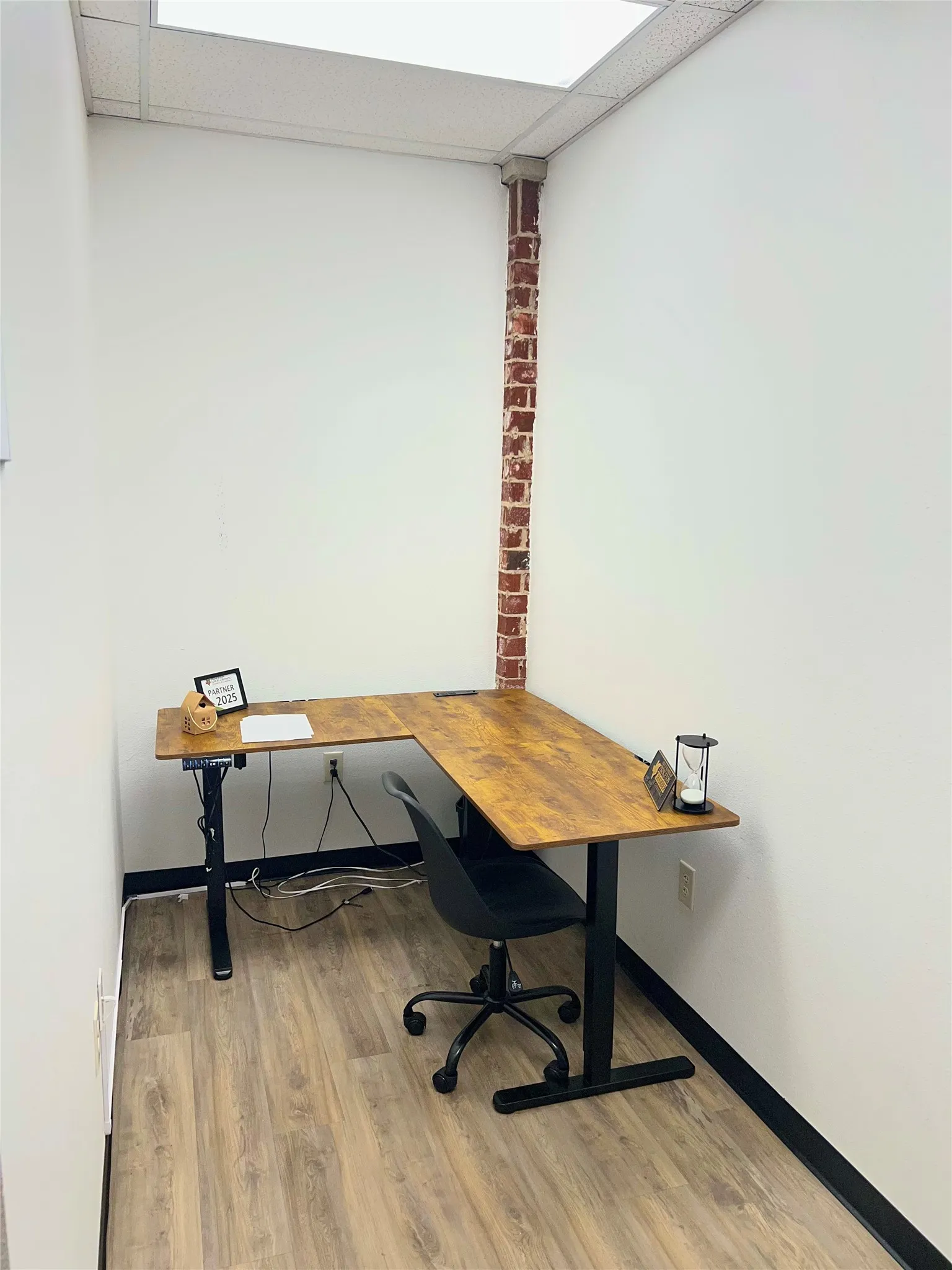 Wood-finish flooring with black trim, white walls, and exposed brick column