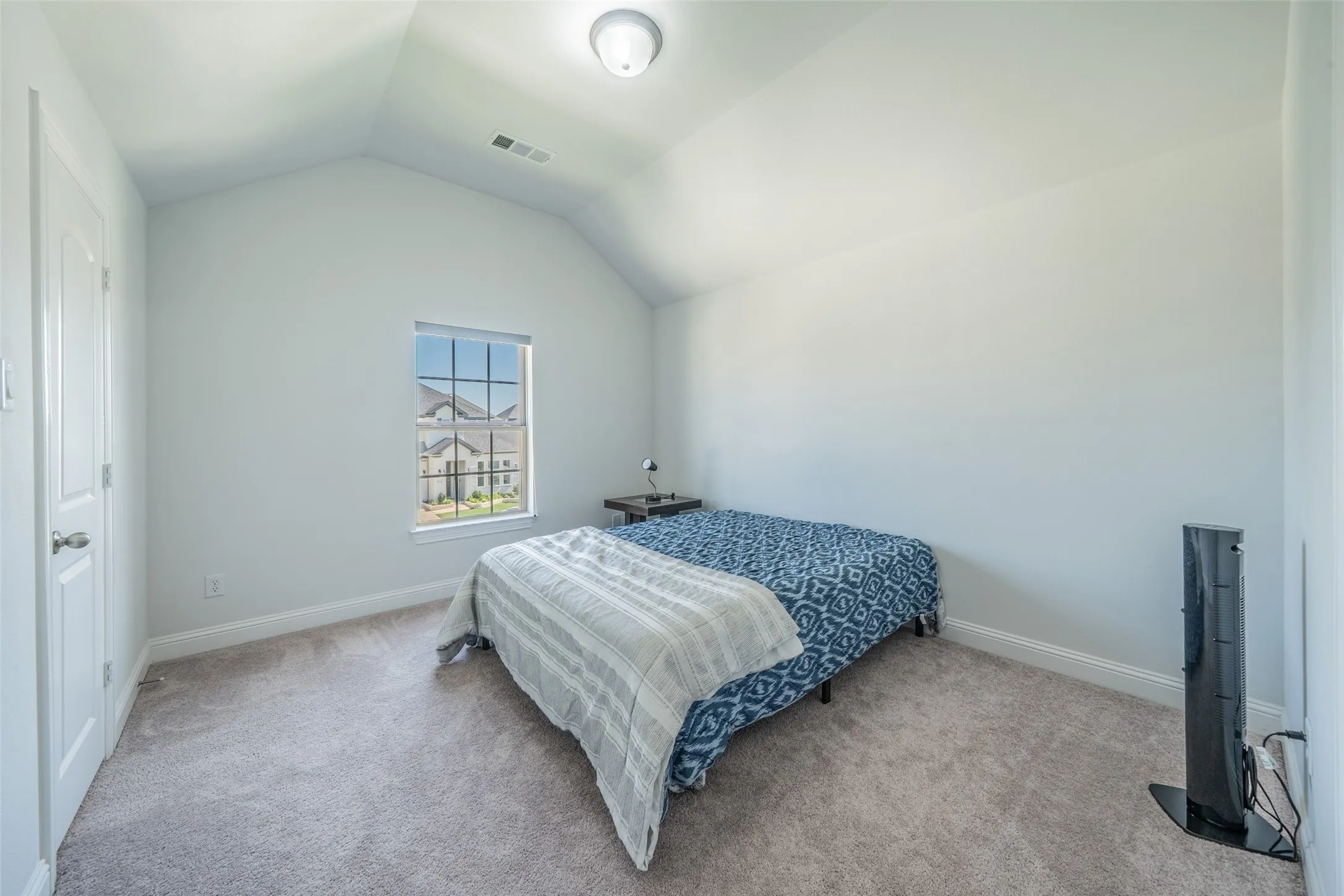 Vaulted ceiling with an overhead light fixture, single window with grid pattern, and carpet flooring
