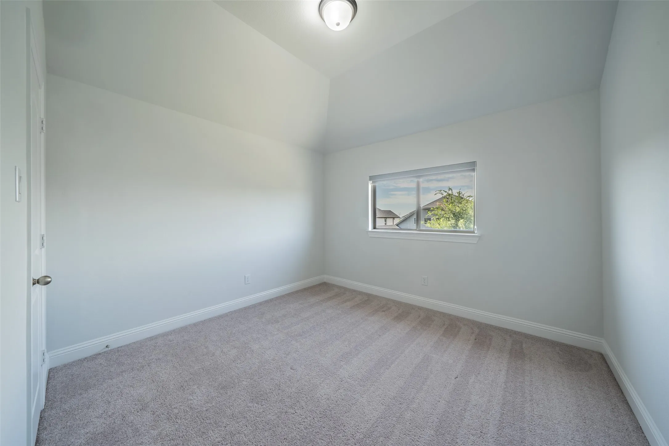 Neutral tone wall paint, vaulted ceiling, and light-toned carpet flooring