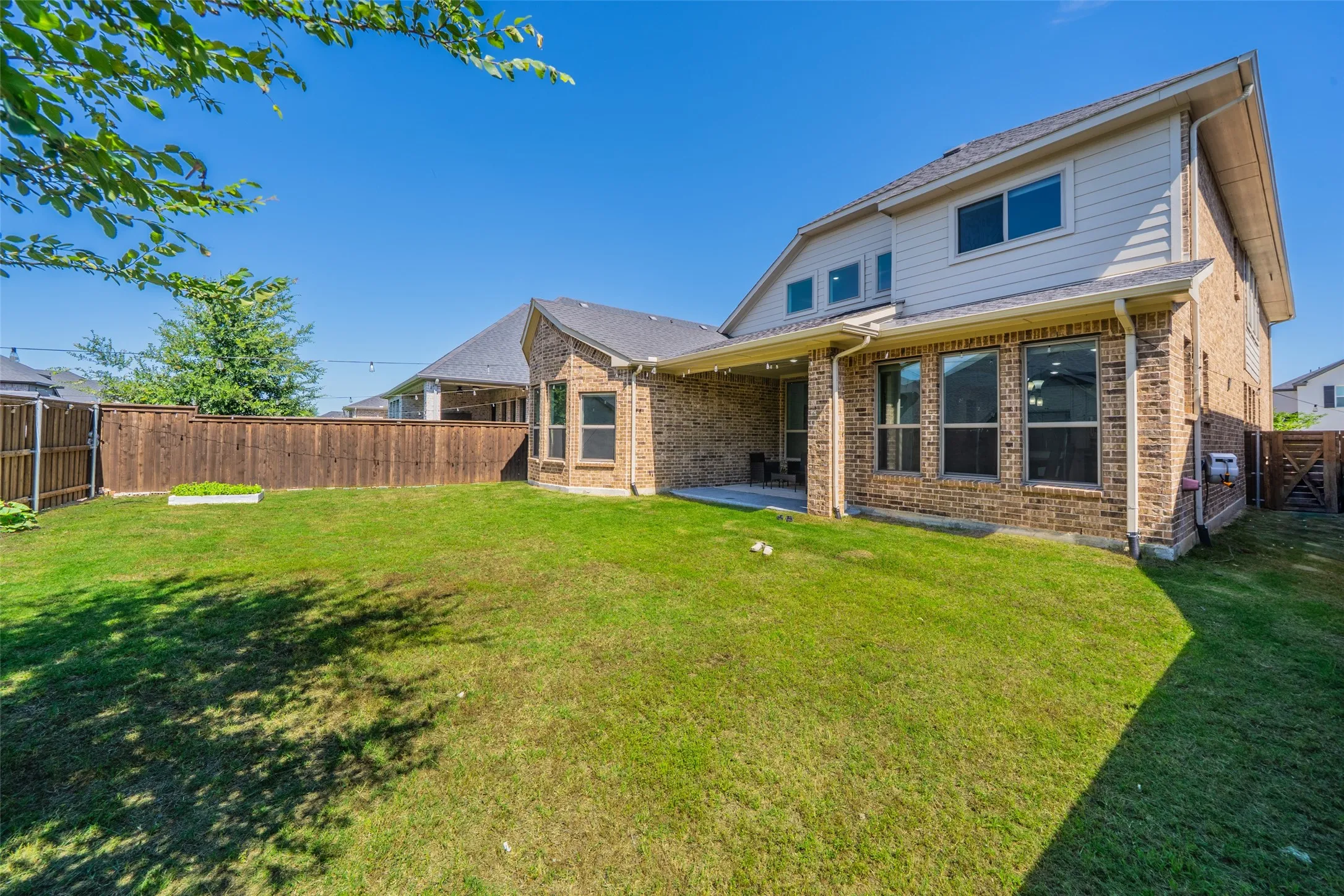 Expansive backyard featuring a green lawn, wood fence, and a covered patio