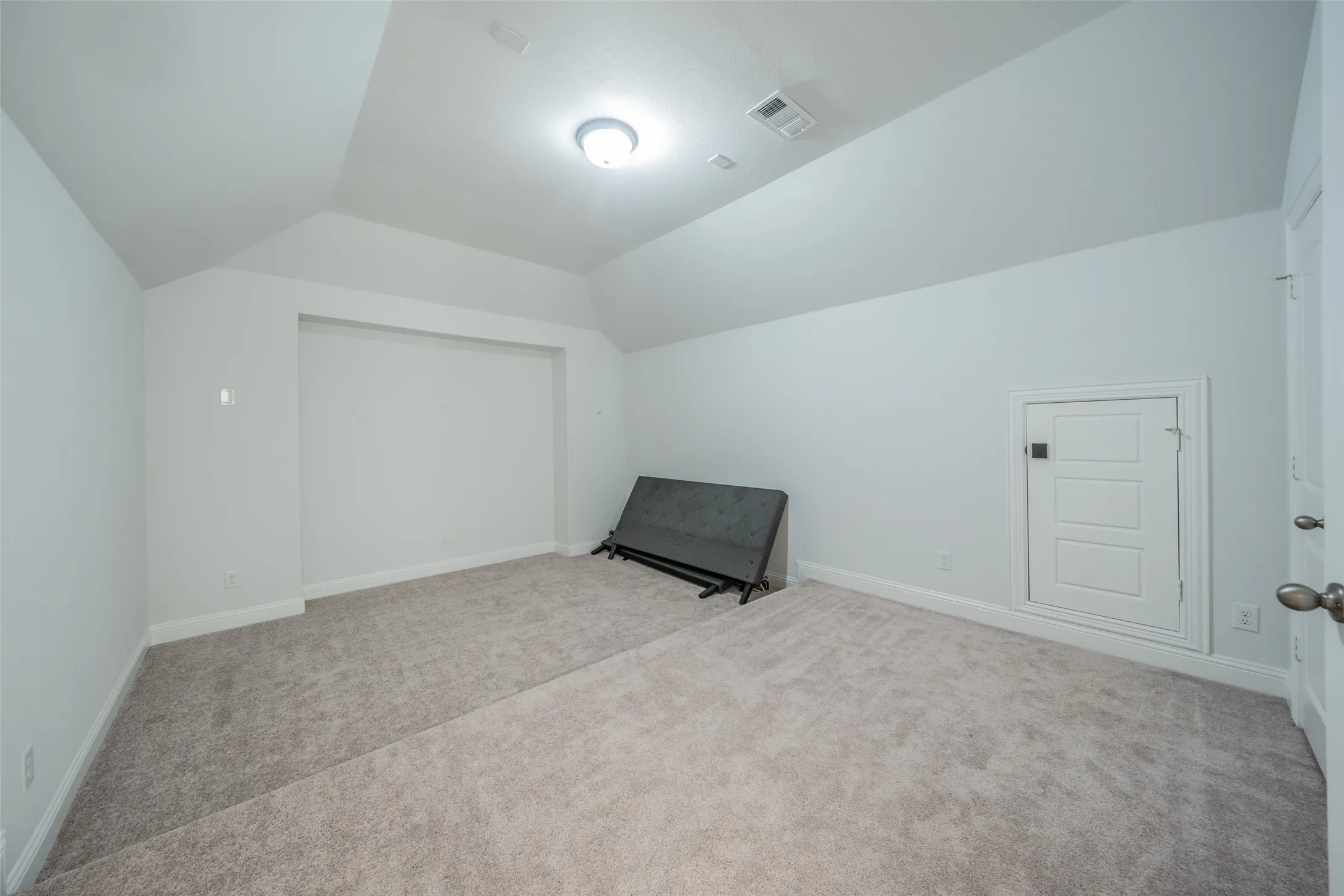 Spacious room featuring vaulted ceilings, recessed wall niche, light gray carpeting, and a panel door with dark hardware