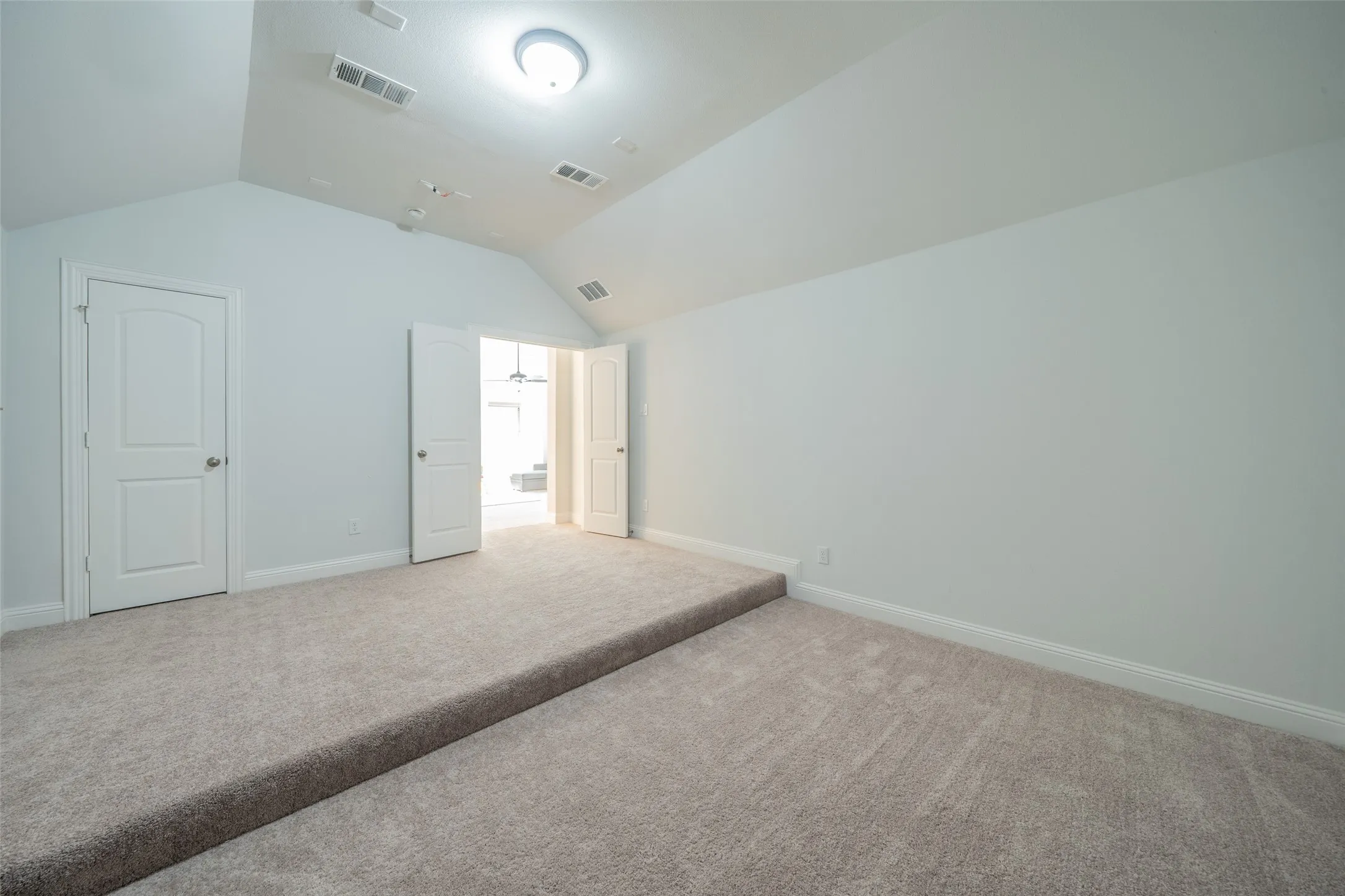 Vaulted ceiling, recessed lighting, neutral carpet, white trim, and a two-panel interior door