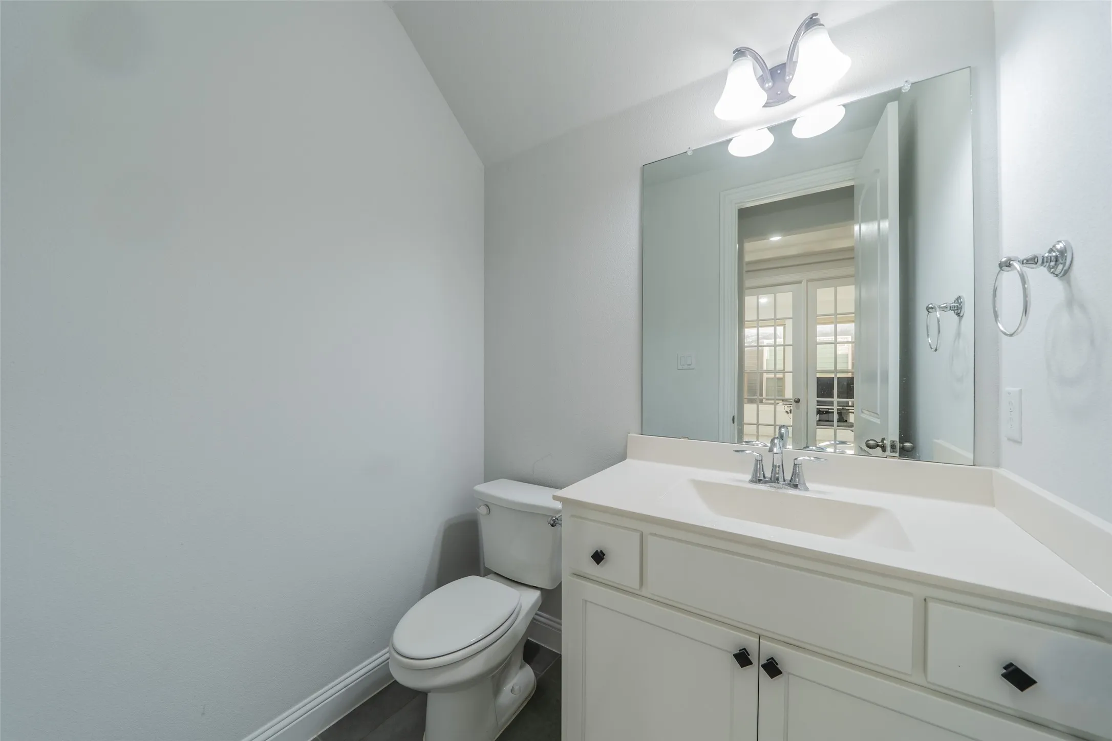 White vanity with a built-in sink, chrome faucet, and rectangular mirror, complemented by a two-light vanity fixture