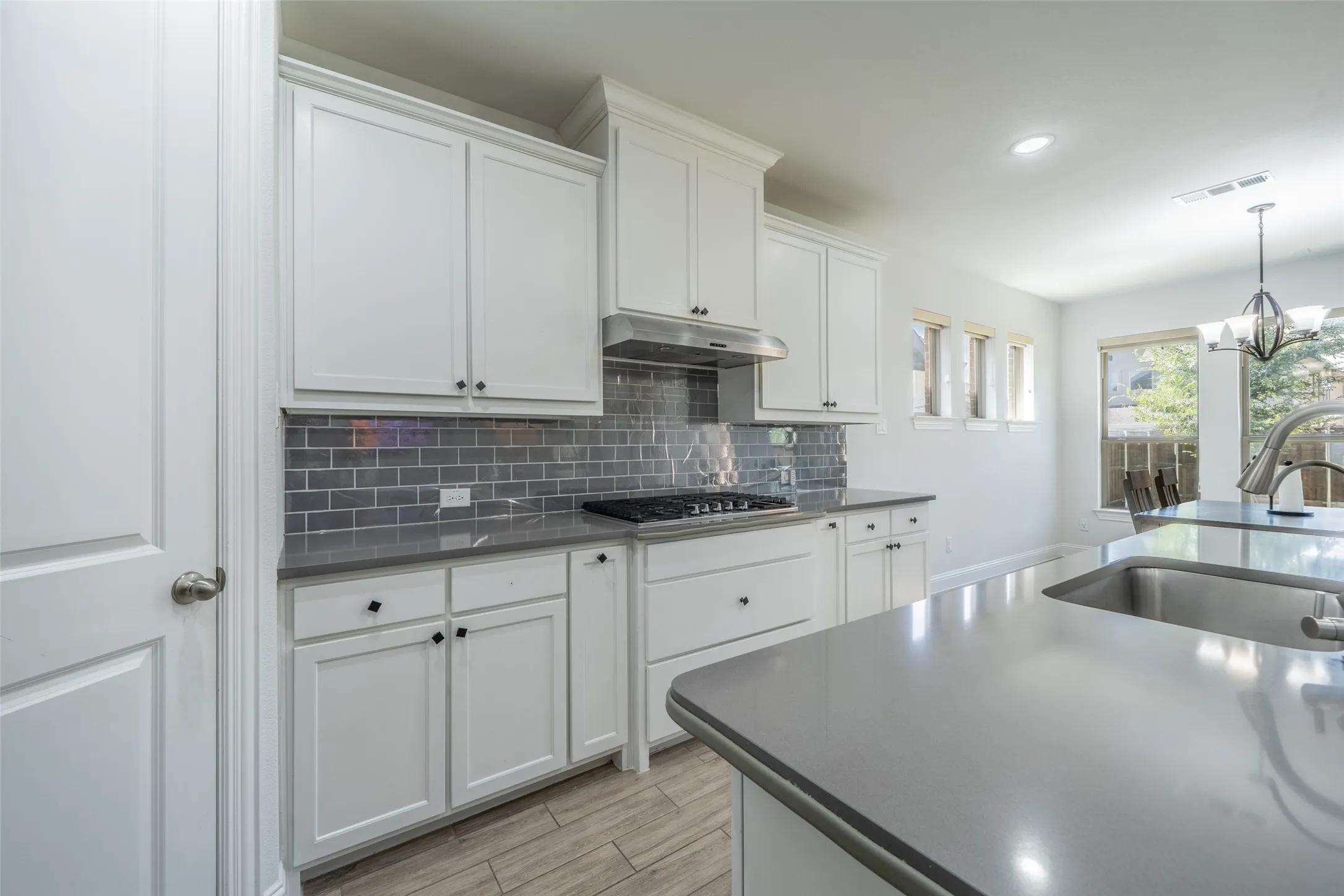 White cabinetry, gray subway tile backsplash, stainless steel gas range, integrated sink, and wood-finish flooring