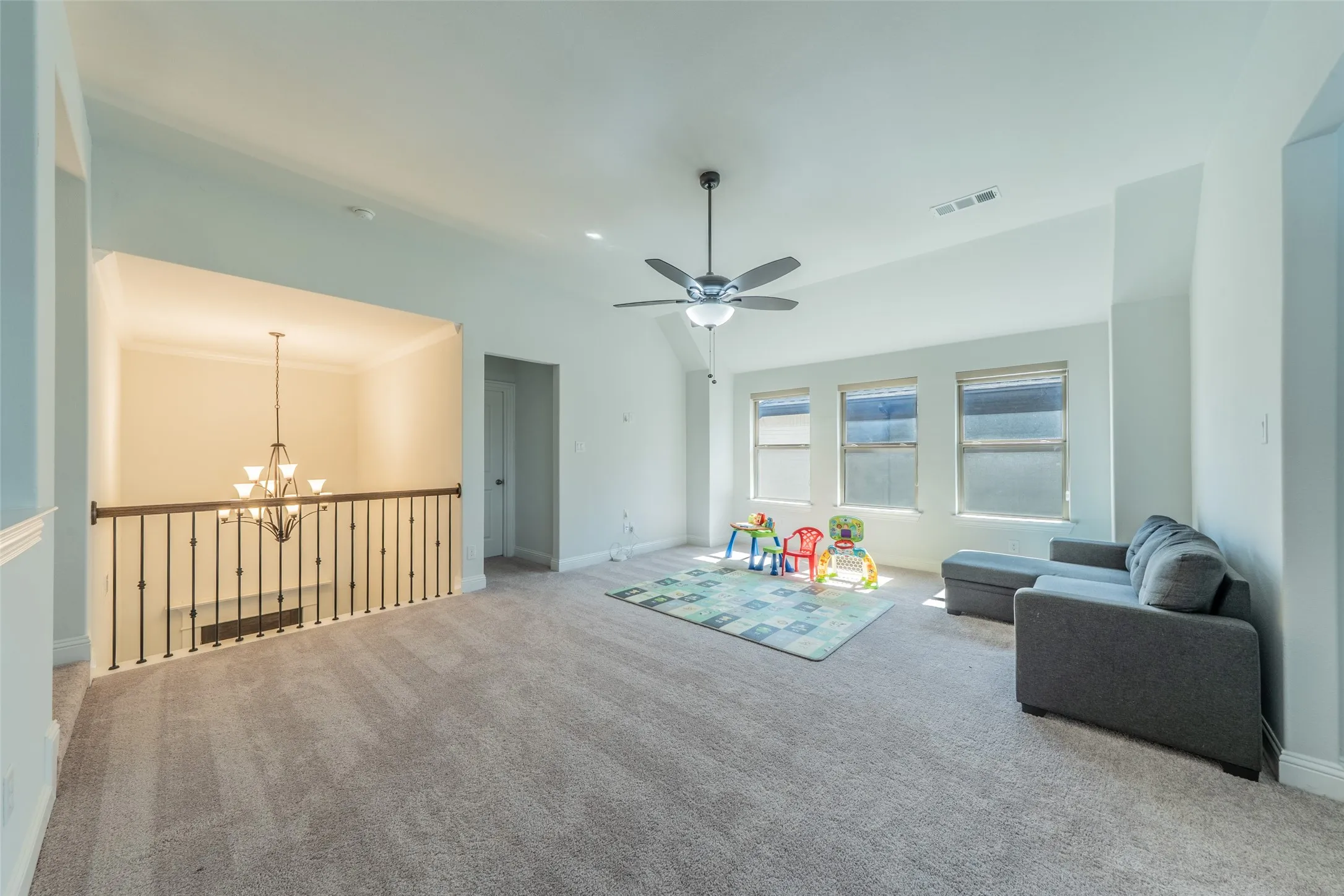 Spacious carpeted room featuring a sloped ceiling, contemporary ceiling fan, and three windows with roller shades