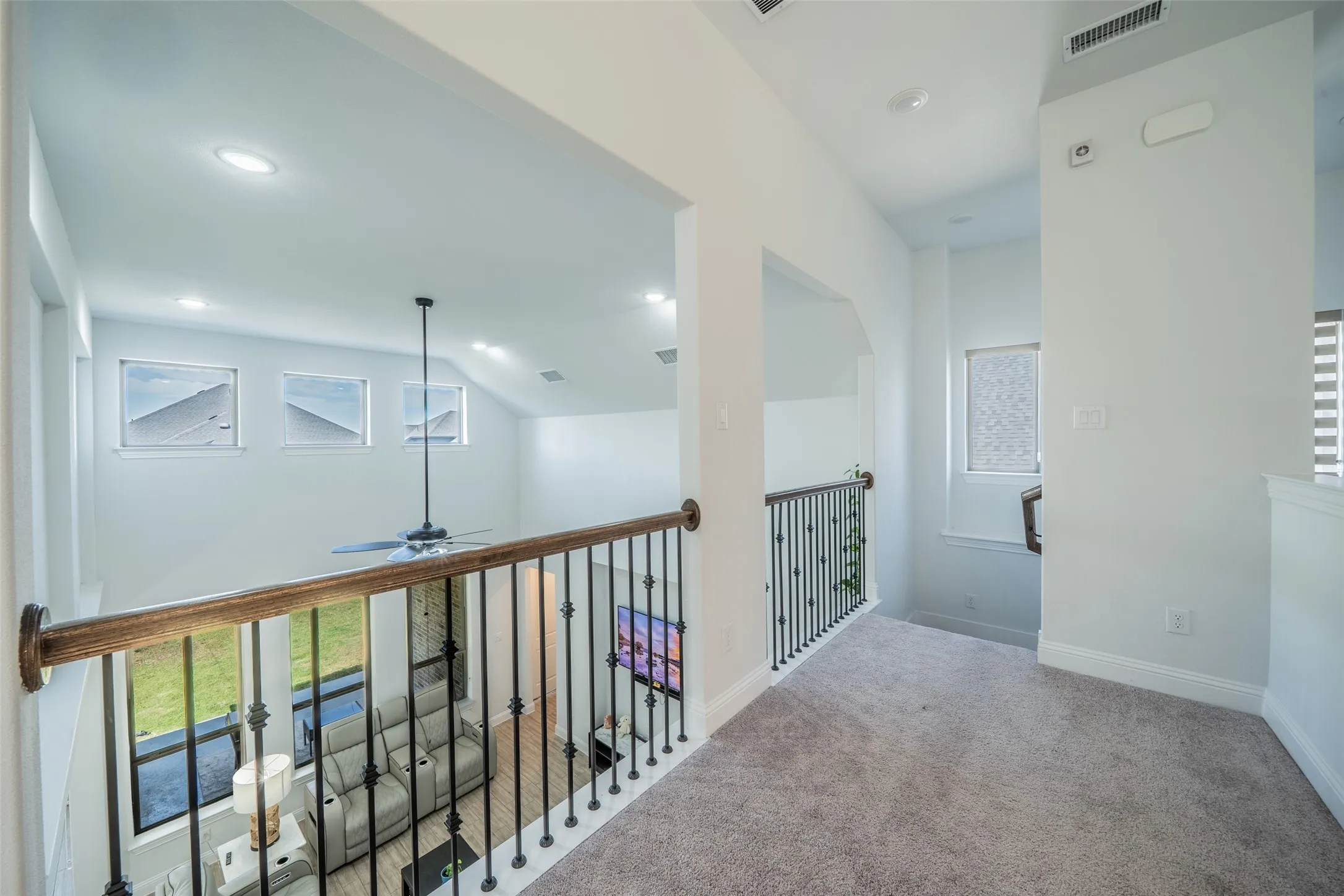 Upper level hallway with carpet flooring and wrought iron balusters