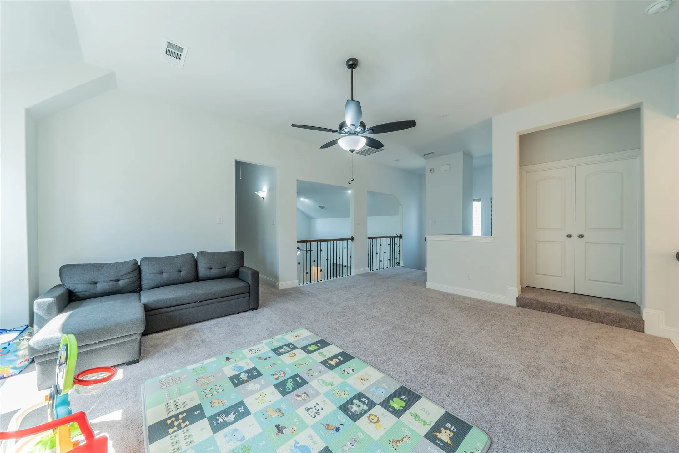 Spacious room featuring vaulted ceilings, carpet flooring, a ceiling fan with integrated lighting, and white double doors