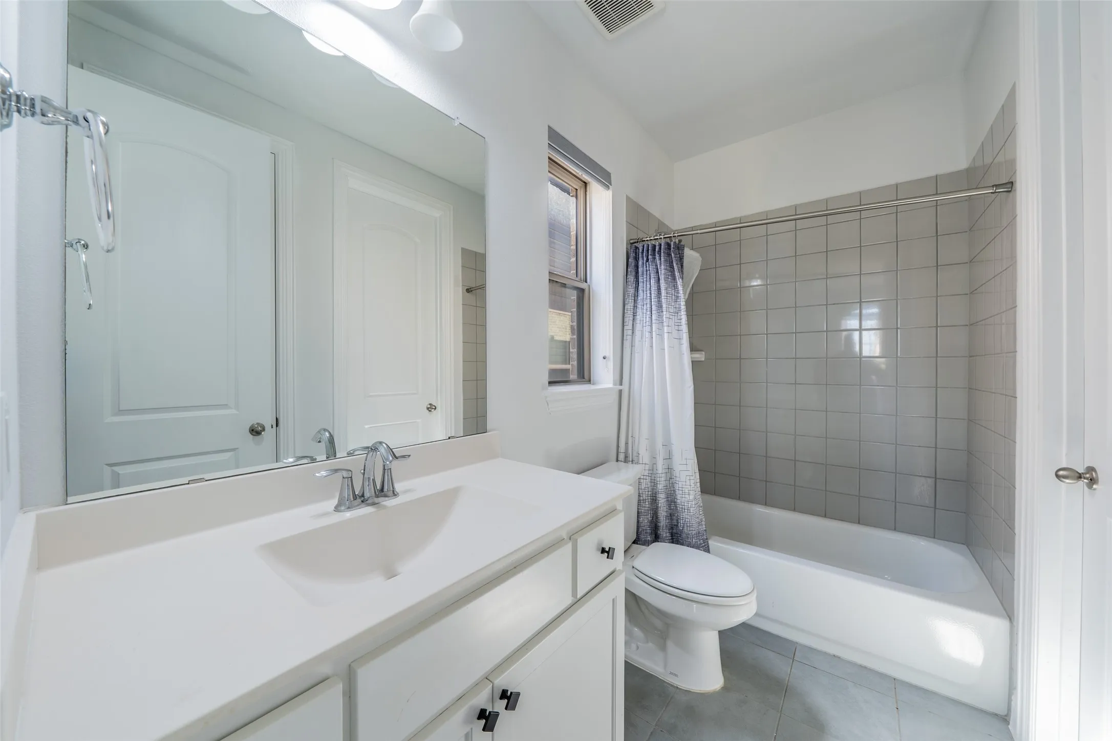 Bathroom featuring a vanity with an integrated sink, a large wall-mounted mirror, a tub/shower combination with tile surround, and tile flooring