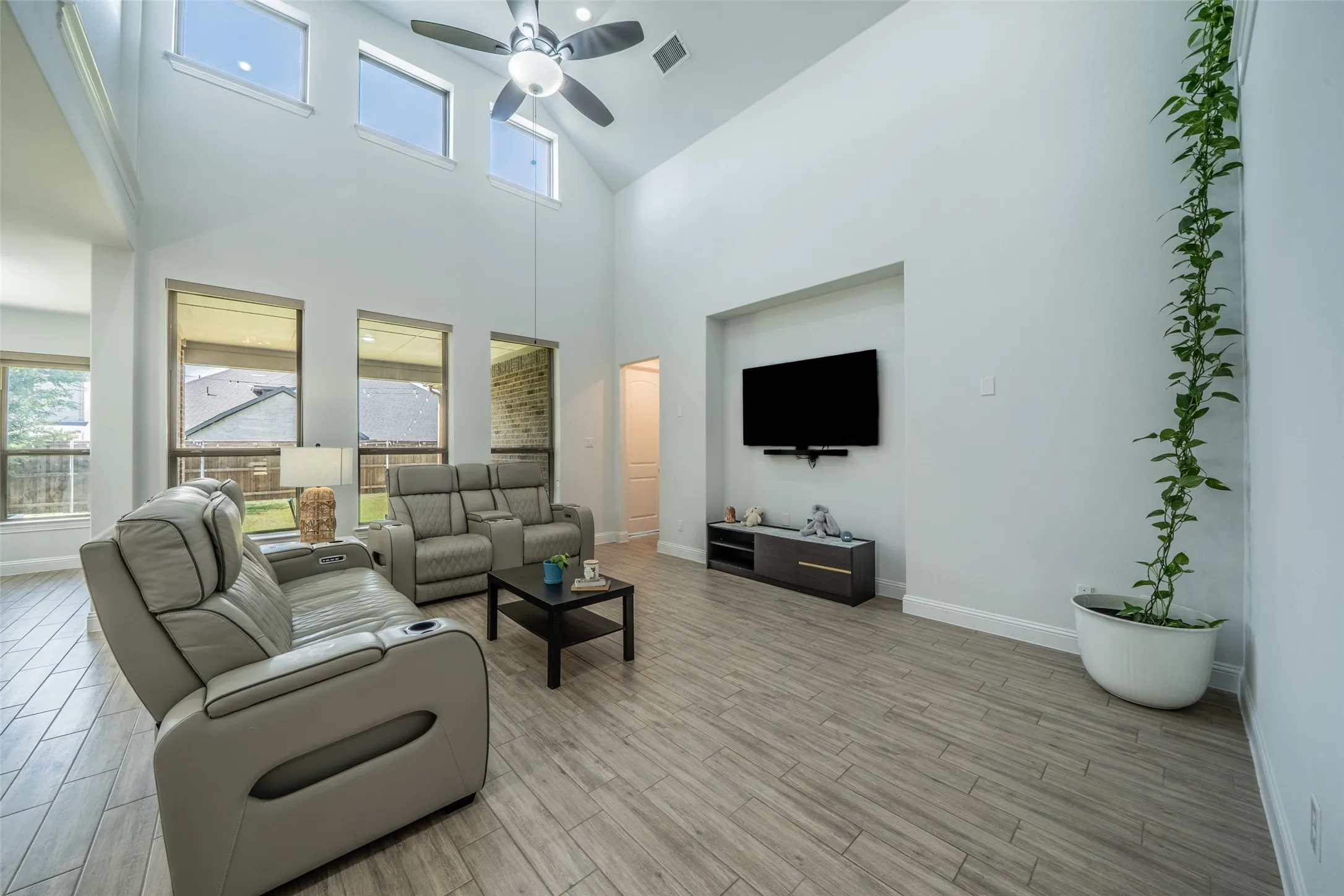 Vaulted ceilings with high windows, wood-finish flooring, recessed wall niche, and ceiling fan with integrated lighting