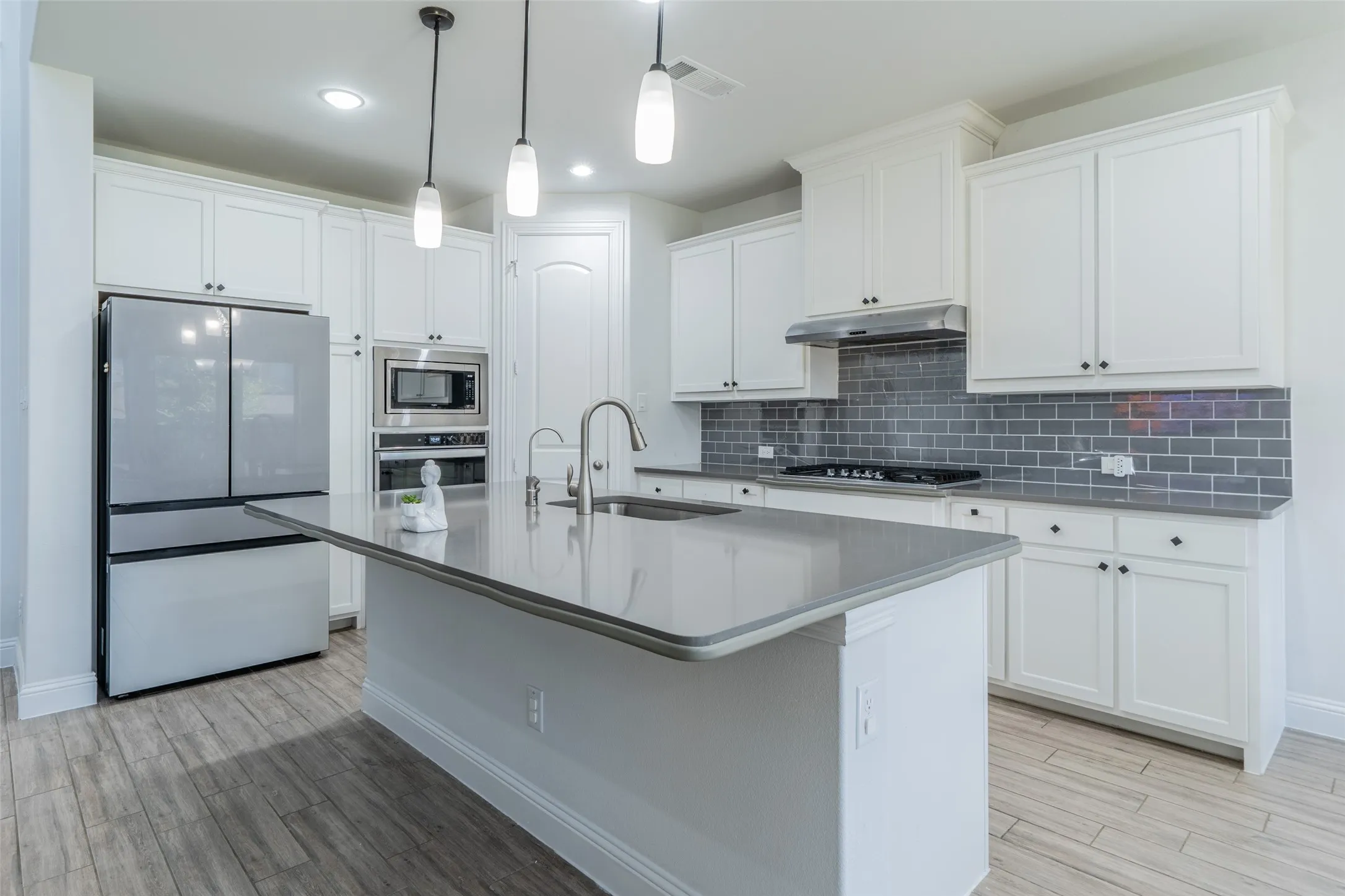 Kitchen featuring an island with a built-in sink, stainless steel appliances, white cabinetry, subway tile backsplash, and wood-finish flooring