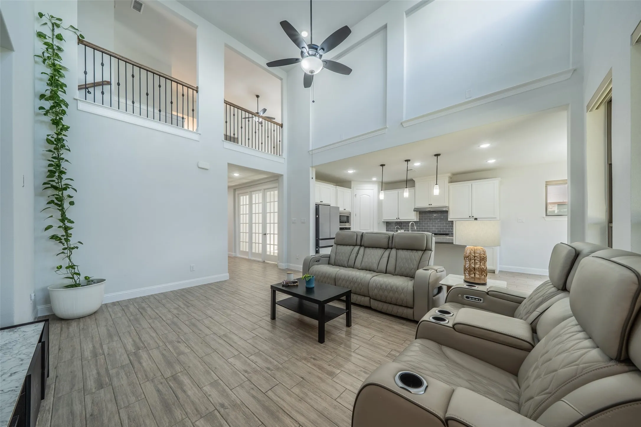 Vaulted ceilings with a ceiling fan, wood-finish flooring, an open-concept layout, a kitchen with white cabinetry and pendant lighting, and French doors
