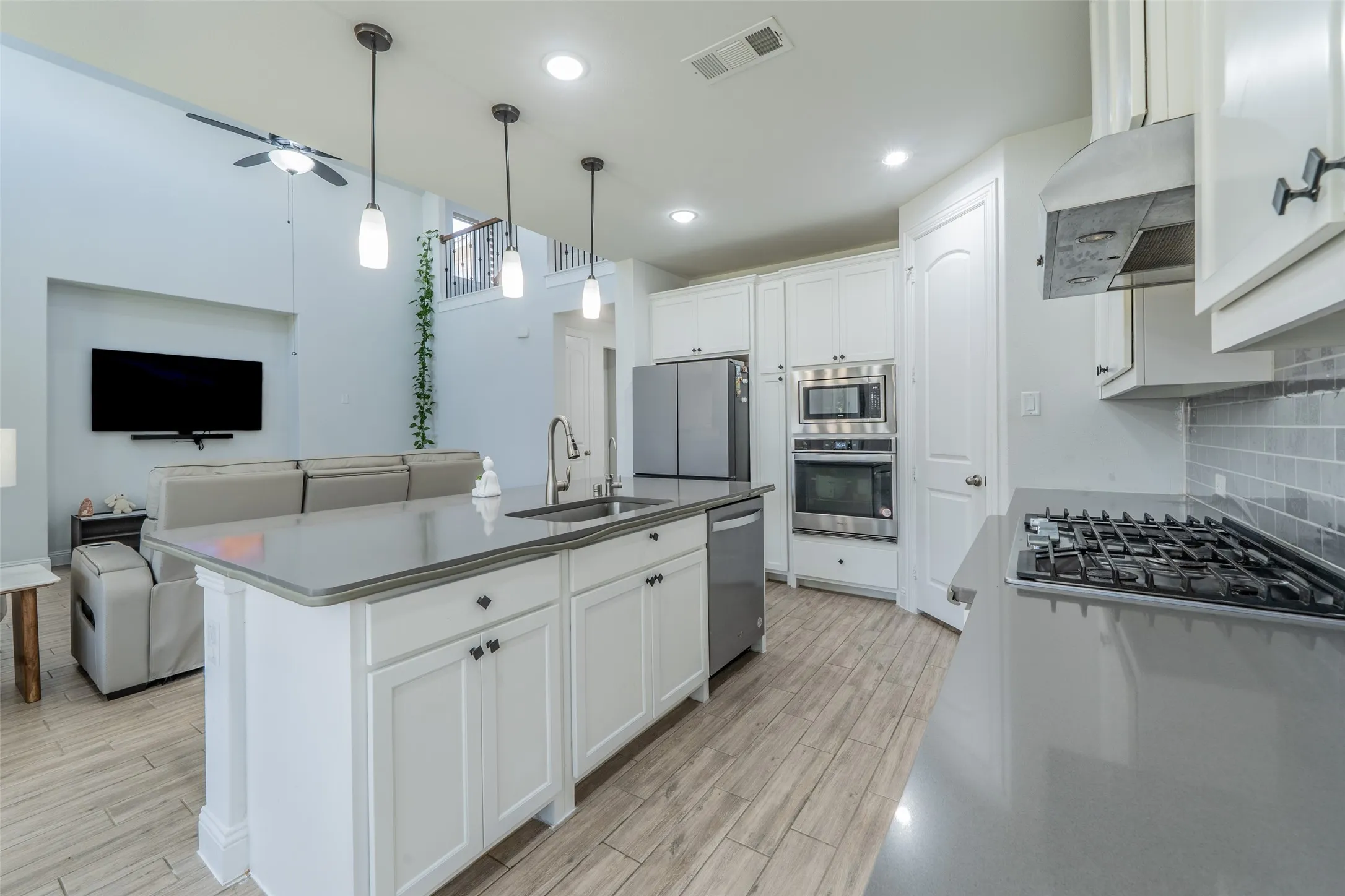 Kitchen featuring light wood-finish flooring, white cabinetry, integrated stainless steel appliances, a center island with pendant lighting, and a gas range with a tile backsplash