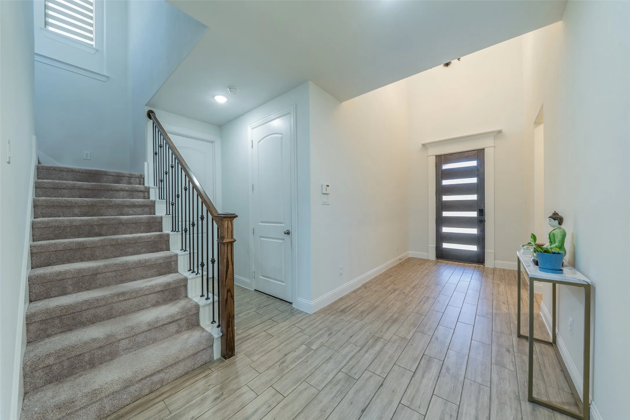 Wood-finish tile flooring, a dark entry door with horizontal glass inserts, and a staircase with wood newel post and wrought iron balusters