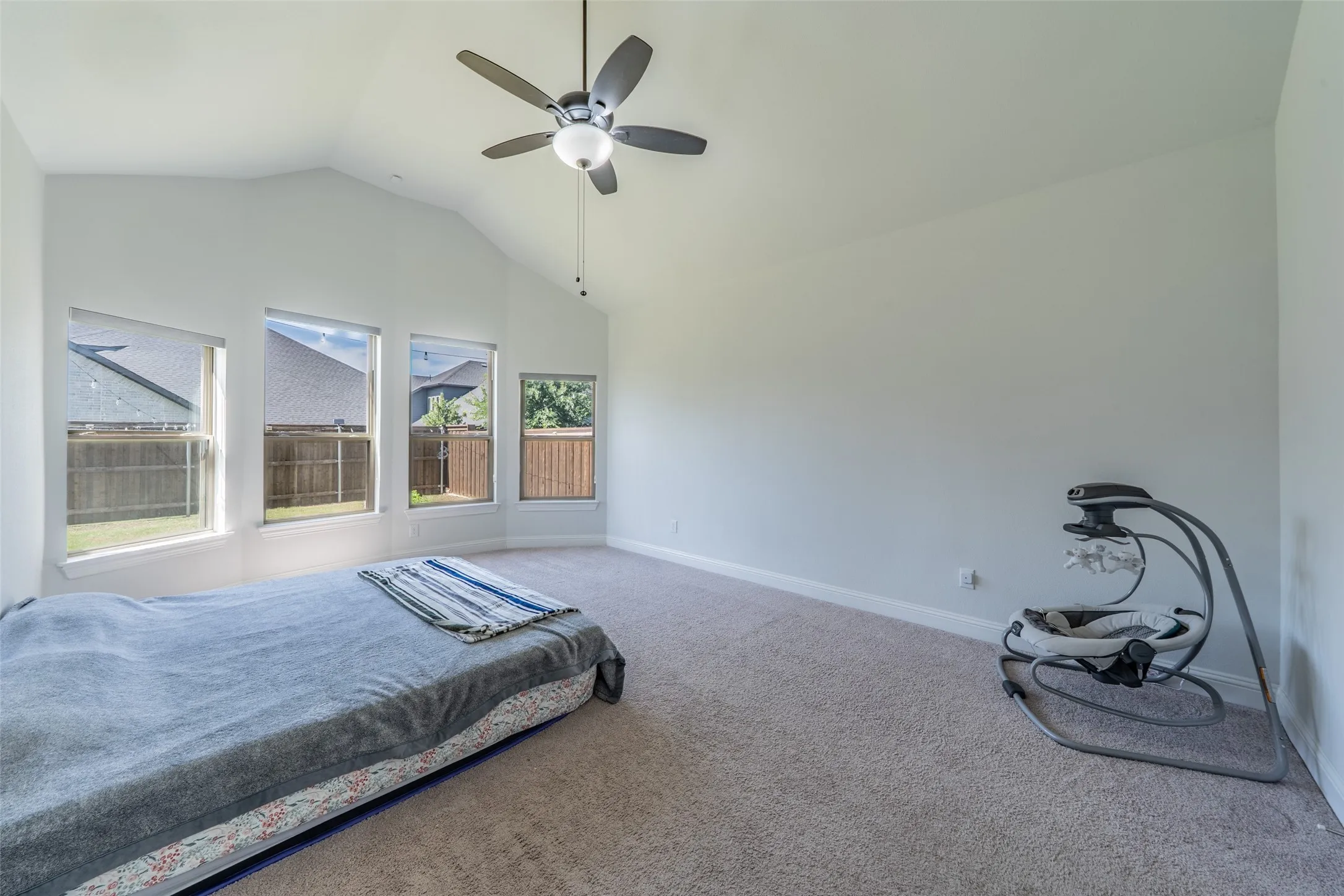 Vaulted ceiling, multiple windows, ceiling fan with integrated lighting, wall-to-wall carpeting, and white painted walls