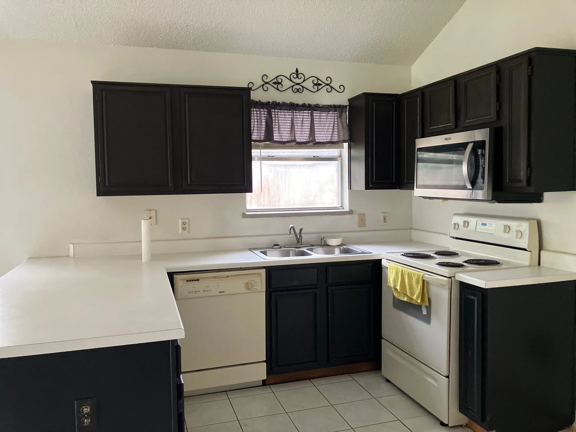 Kitchen featuring black cabinetry, white countertops, stainless steel microwave, and white appliances