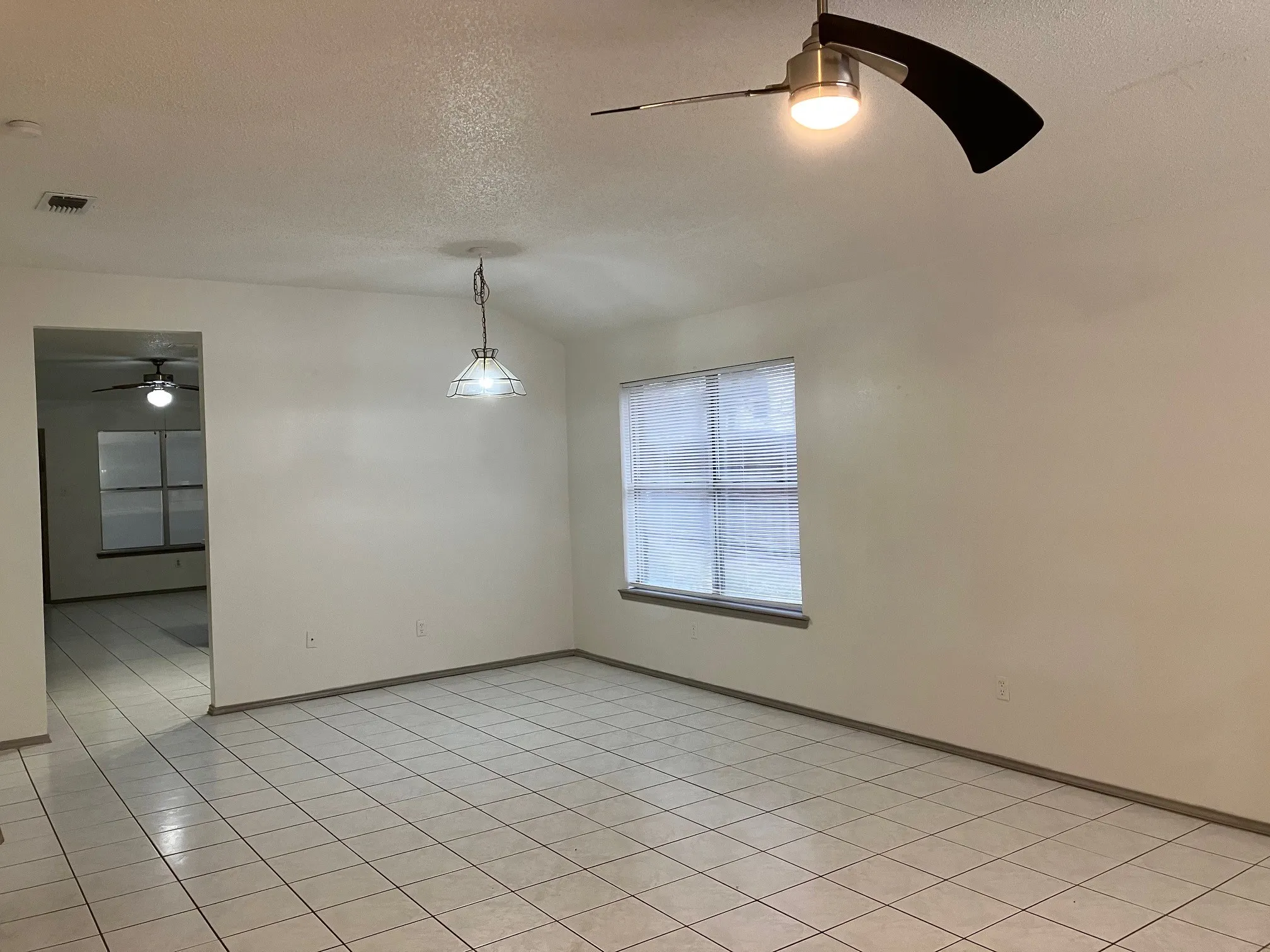 Recessed window with horizontal blinds, overhead ceiling fan with light, pendant light fixture, and tile flooring
