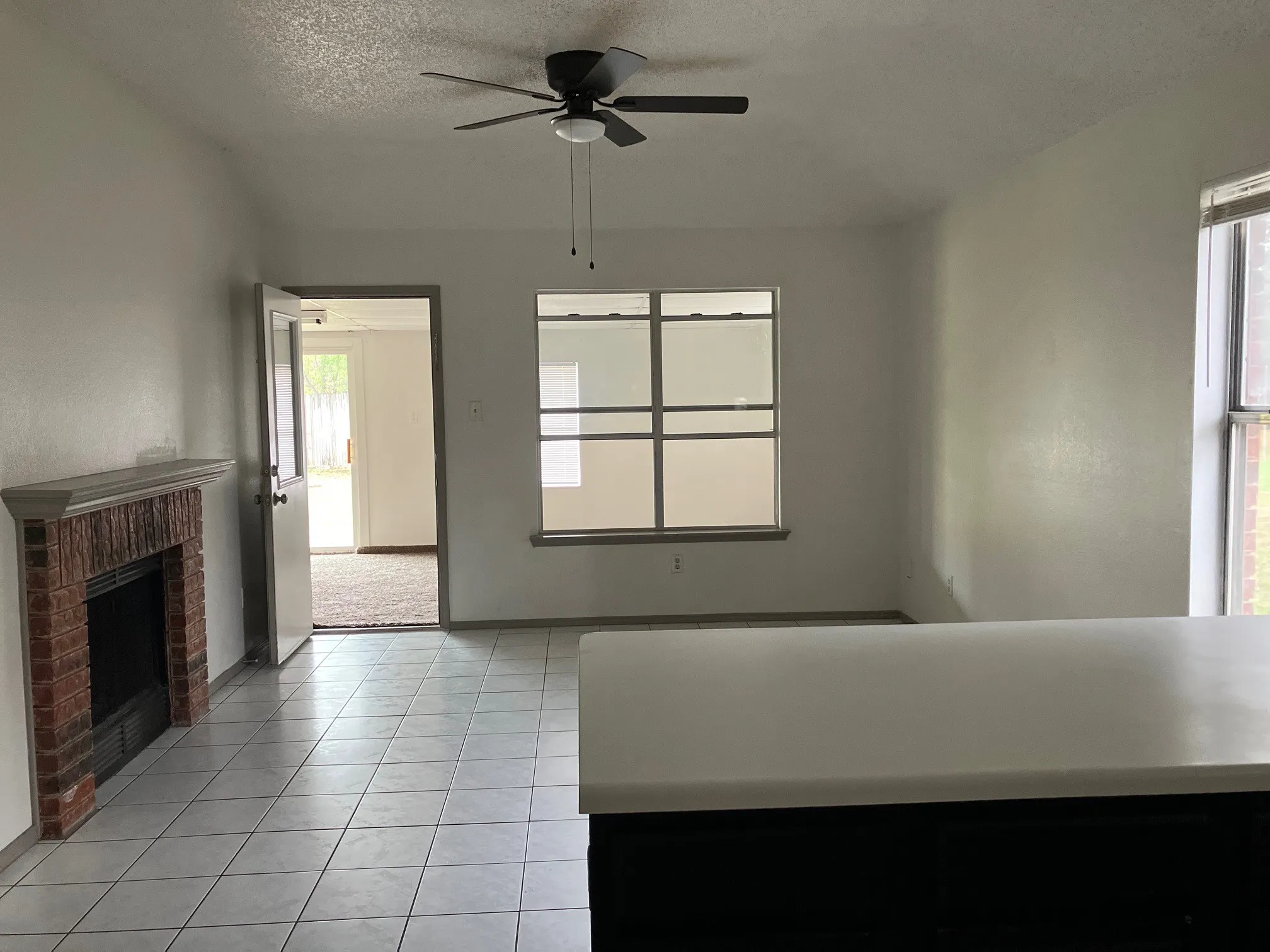 Living space featuring a brick fireplace, tiled flooring, ceiling fan, and a built-in counter with a light-toned surface