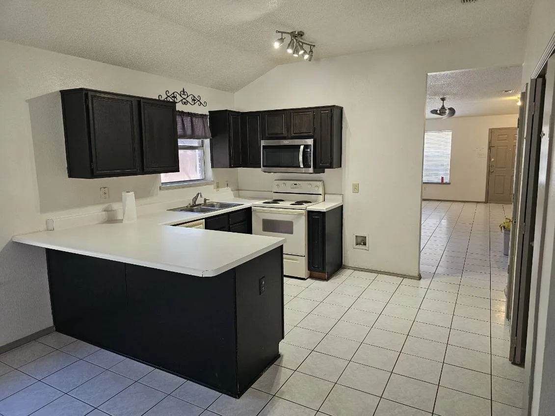 Kitchen featuring dark cabinetry, white countertops, stainless steel microwave, and white tile flooring