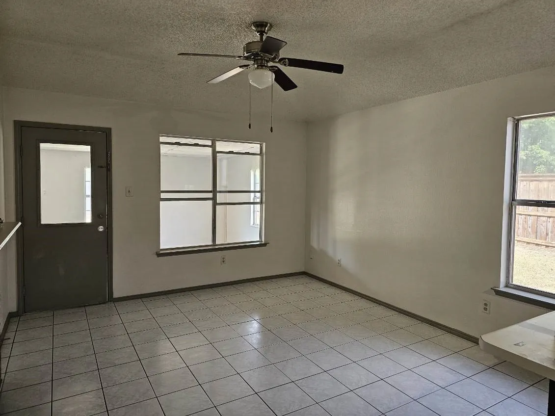 Room featuring large tile flooring, a ceiling fan, and multiple windows