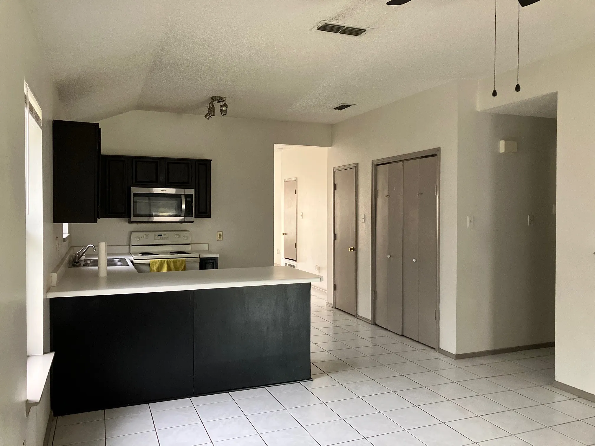 Kitchen area featuring black cabinetry, white countertops, stainless steel microwave, and white tile flooring
