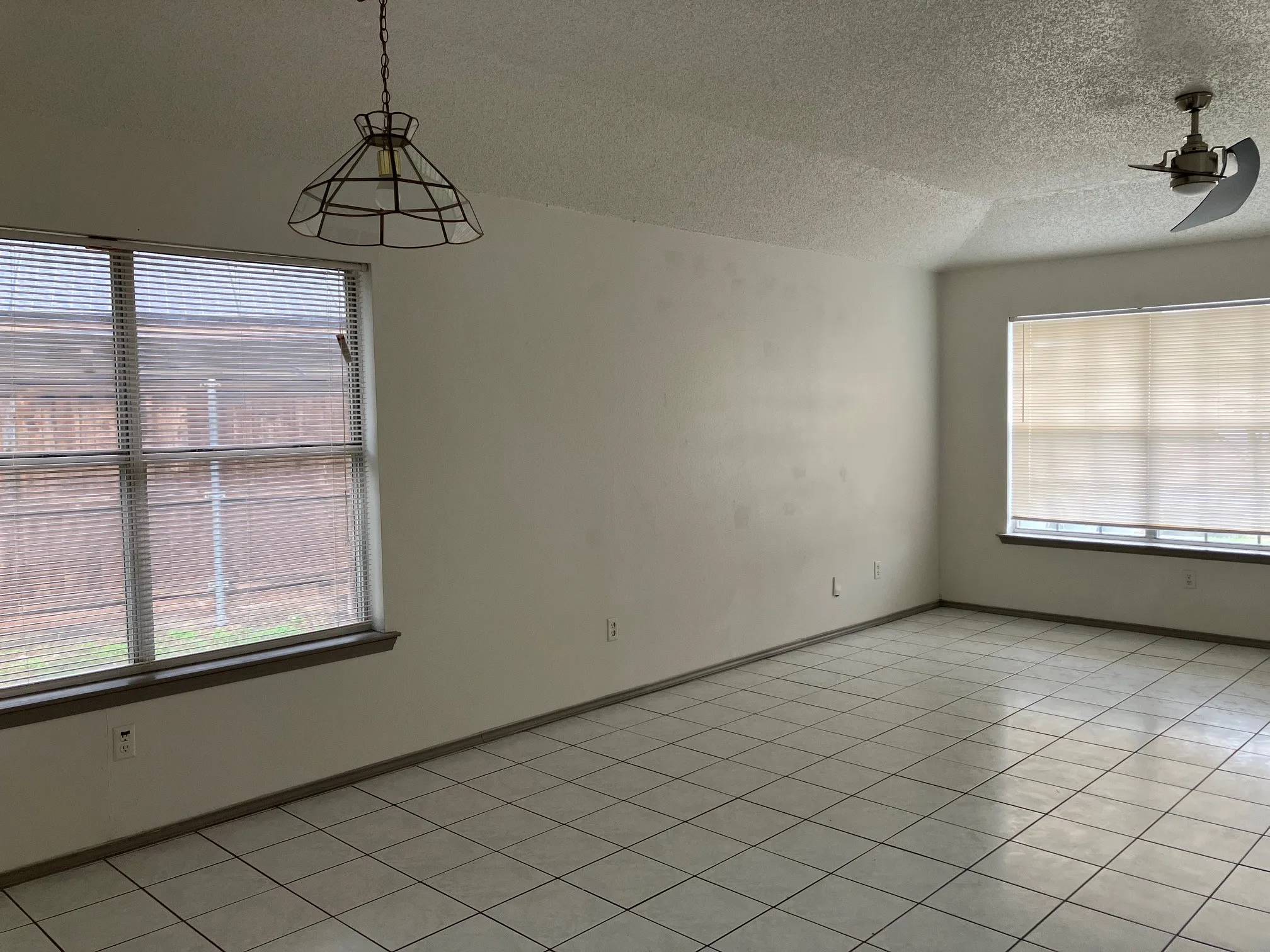 Tiled flooring, vaulted ceiling, large windows with blinds, ceiling fan, and pendant light fixture