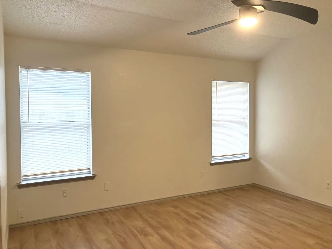 Vaulted ceiling with a ceiling fan, two windows, and wood-finish flooring