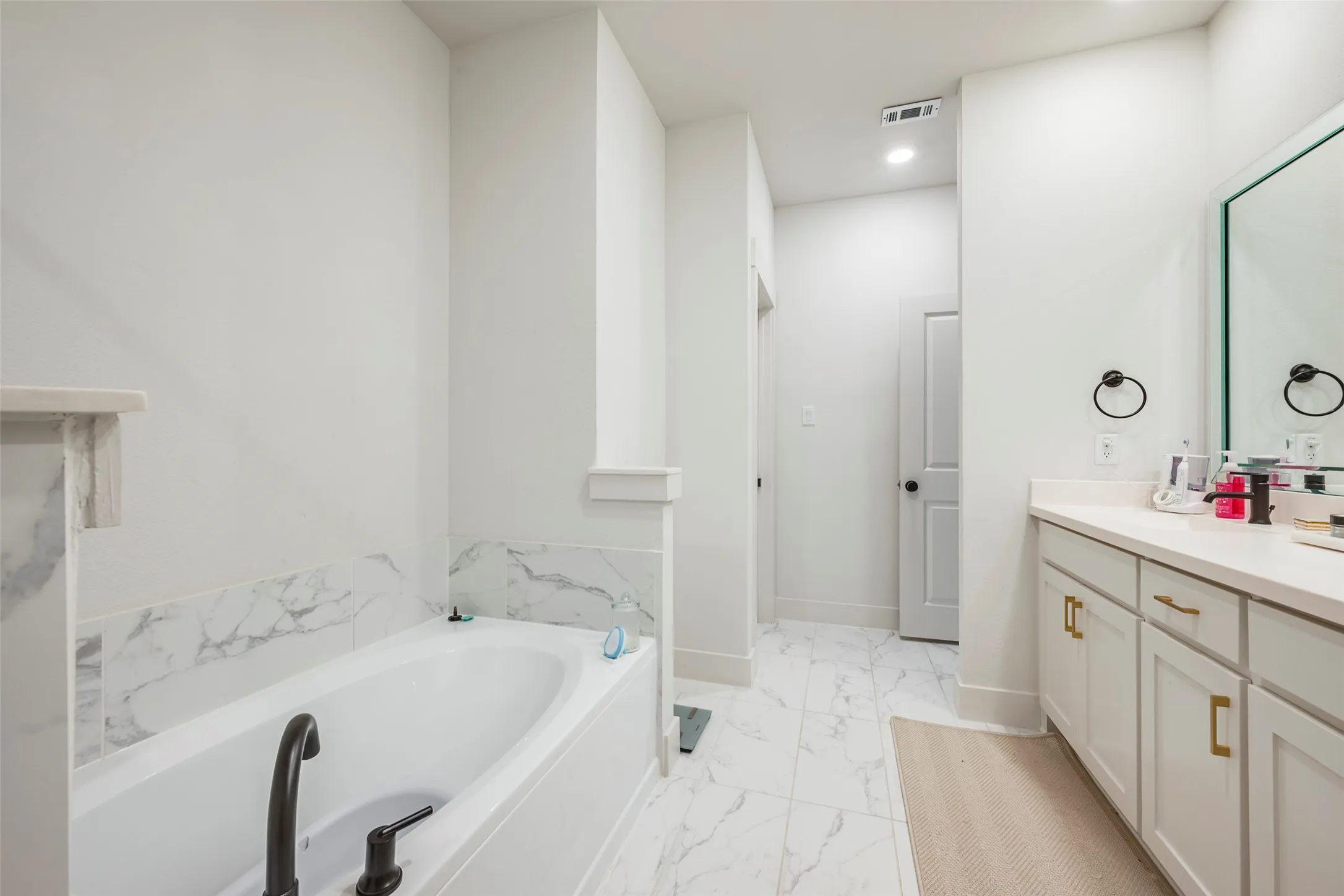 Built-in bathtub with a dark-finish faucet, white vanity with a light-finish countertop, and gold-finish hardware