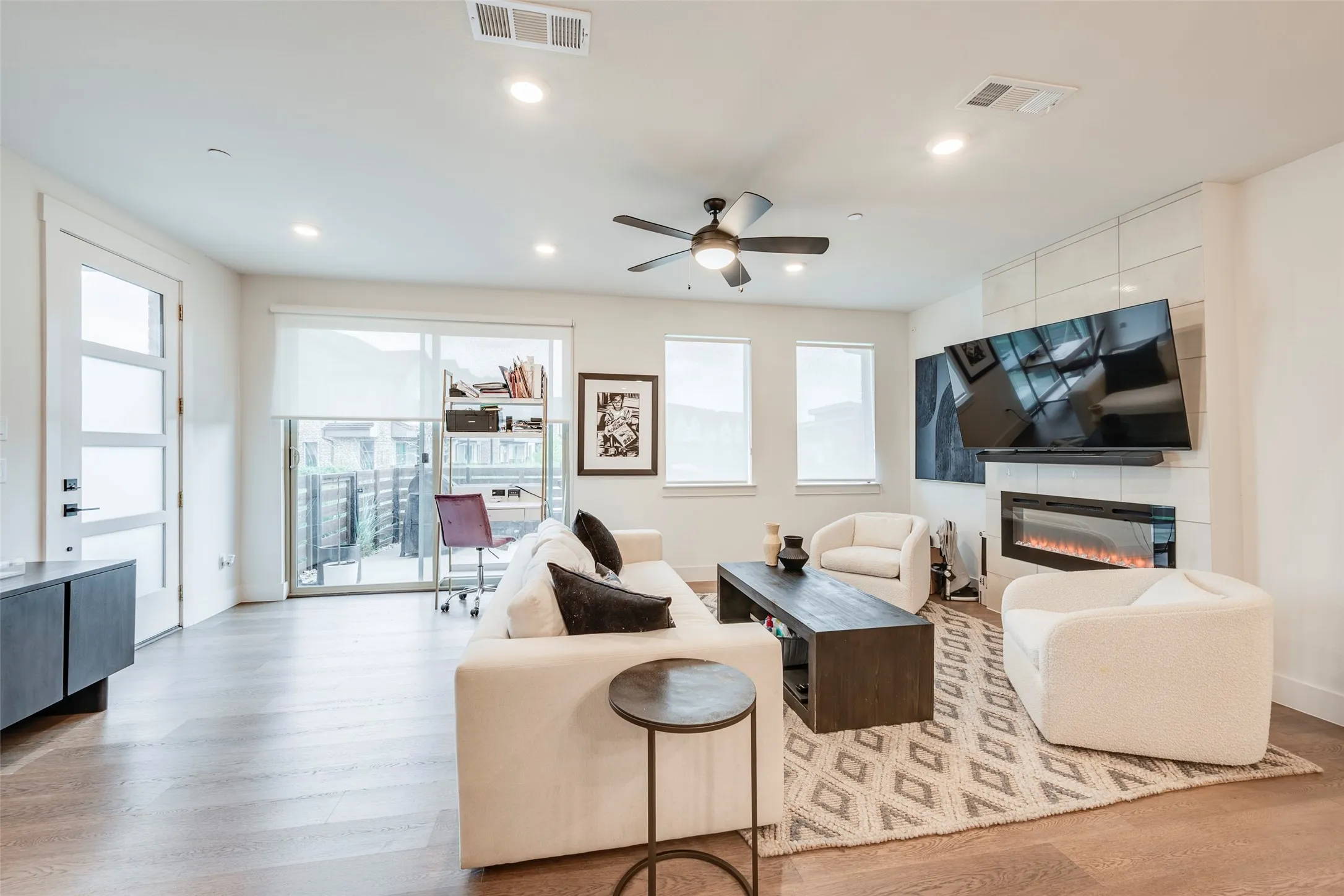 Wood-finish flooring throughout, modern electric fireplace, recessed lighting, ceiling fan, and sliding glass door to exterior