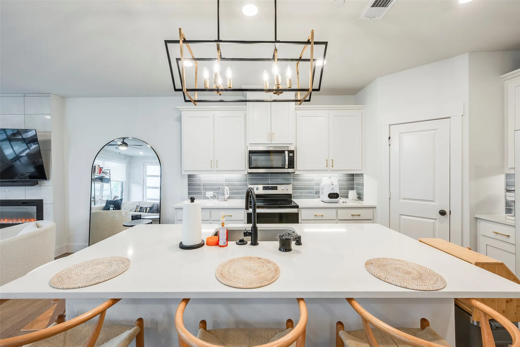 Kitchen island with integrated sink, white cabinetry, tile backsplash, built-in microwave, and electric range