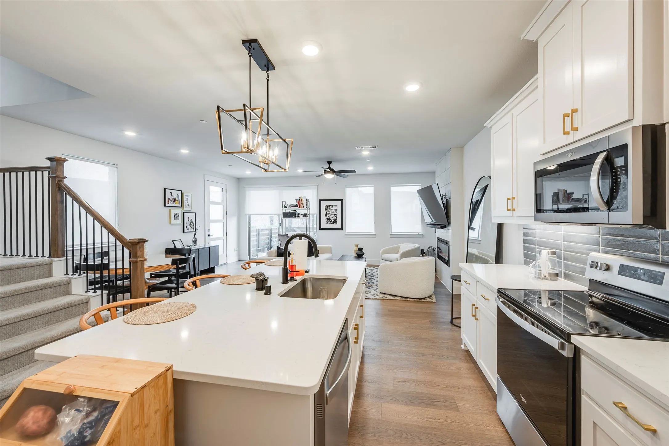 Open-concept living area featuring a kitchen island with sink, stainless steel appliances, wood-finish flooring, and a staircase with metal balusters