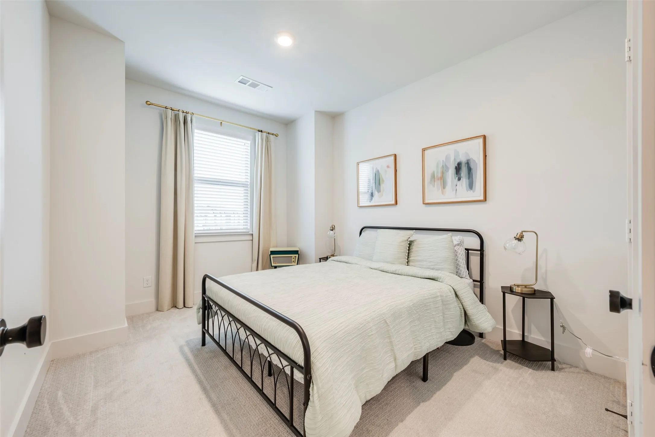 Recessed lighting, light-colored carpeting, a window with blinds, and white walls create a bright interior