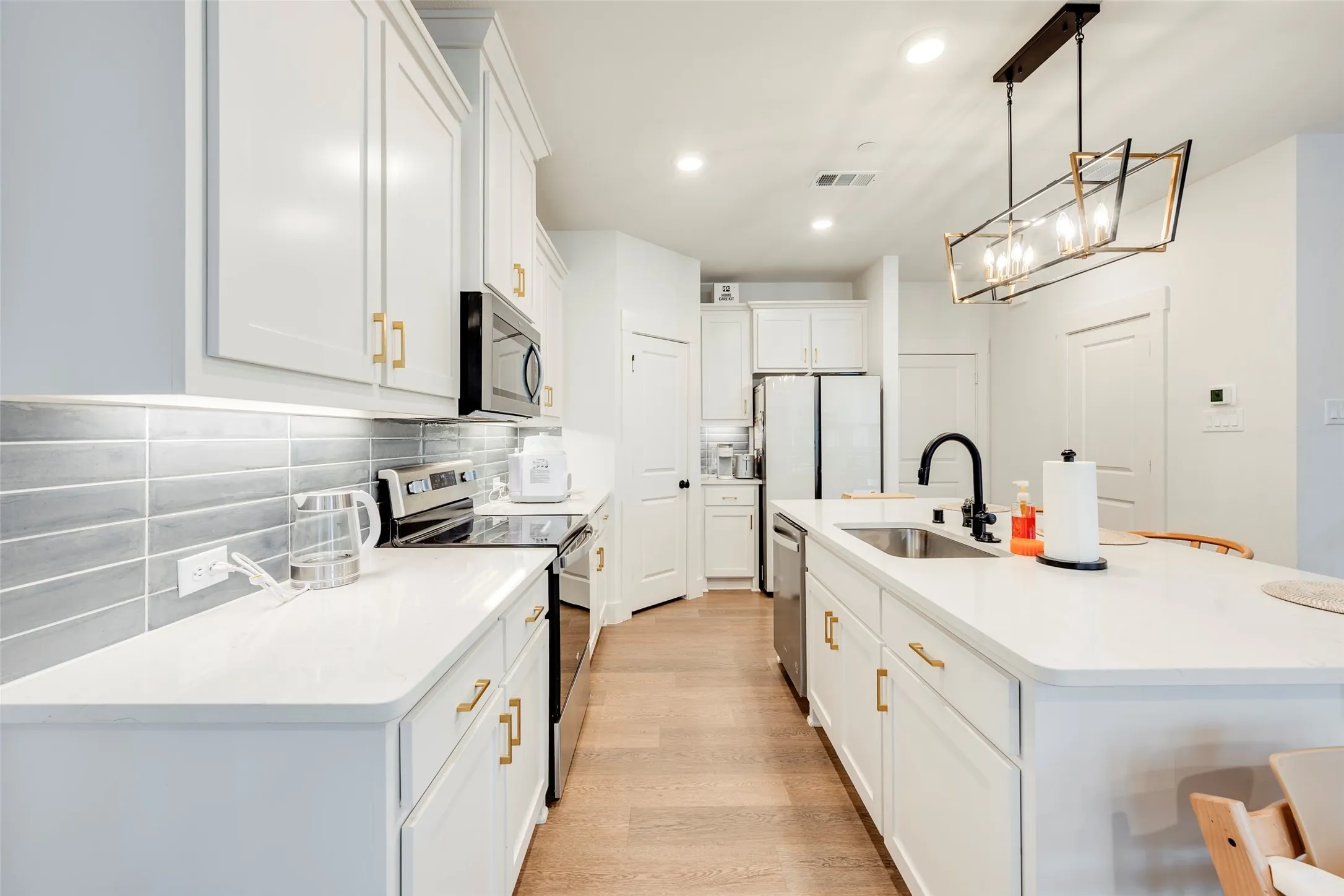 Kitchen featuring white cabinetry, light countertops, stainless steel appliances, a tile backsplash, and a central island with a sink