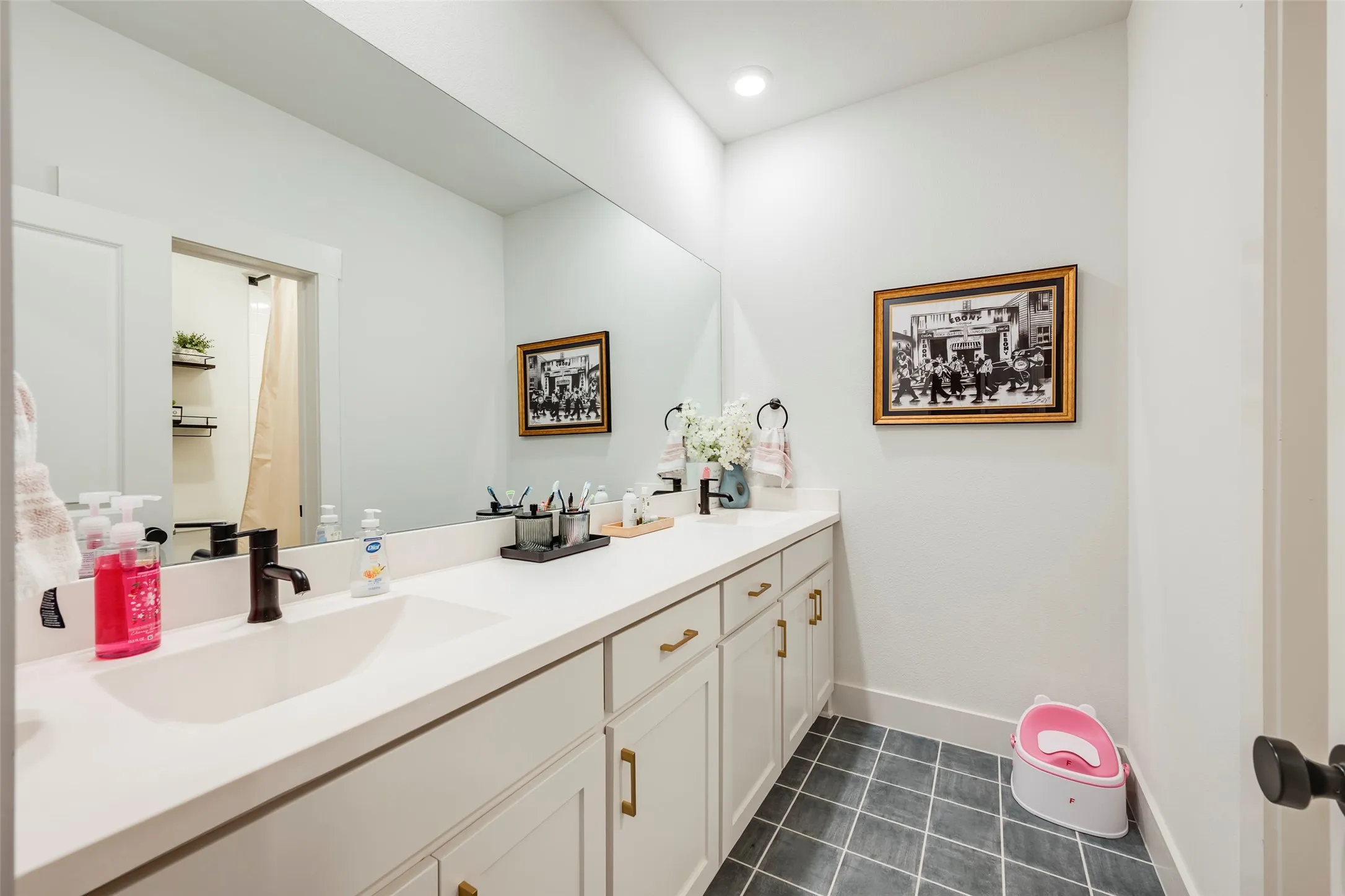 Dual-sink vanity with white countertops, white cabinetry, brass hardware, and dark faucets