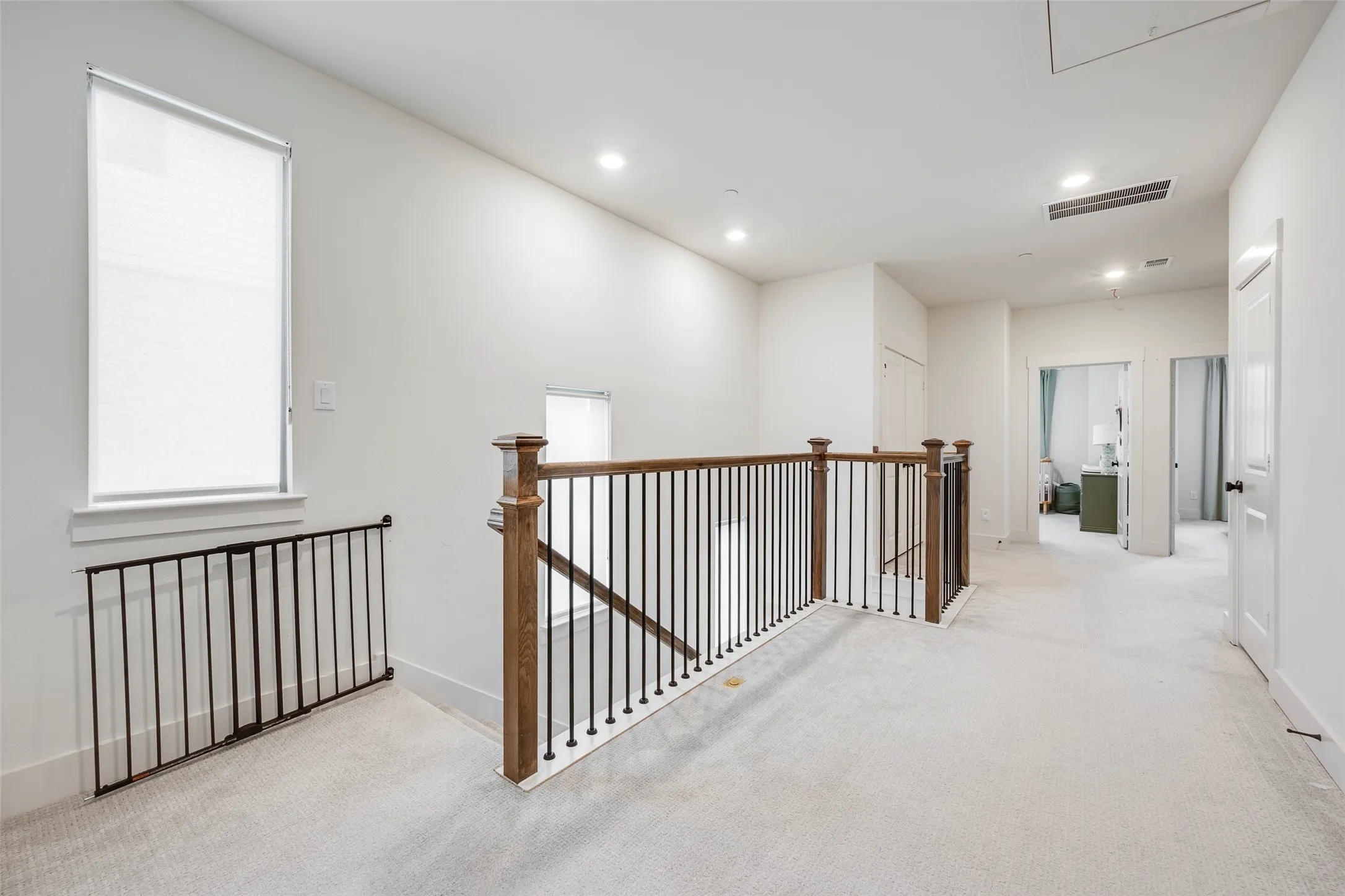 Upper-level landing featuring light-toned carpeting, recessed lighting, and a window with a roller shade